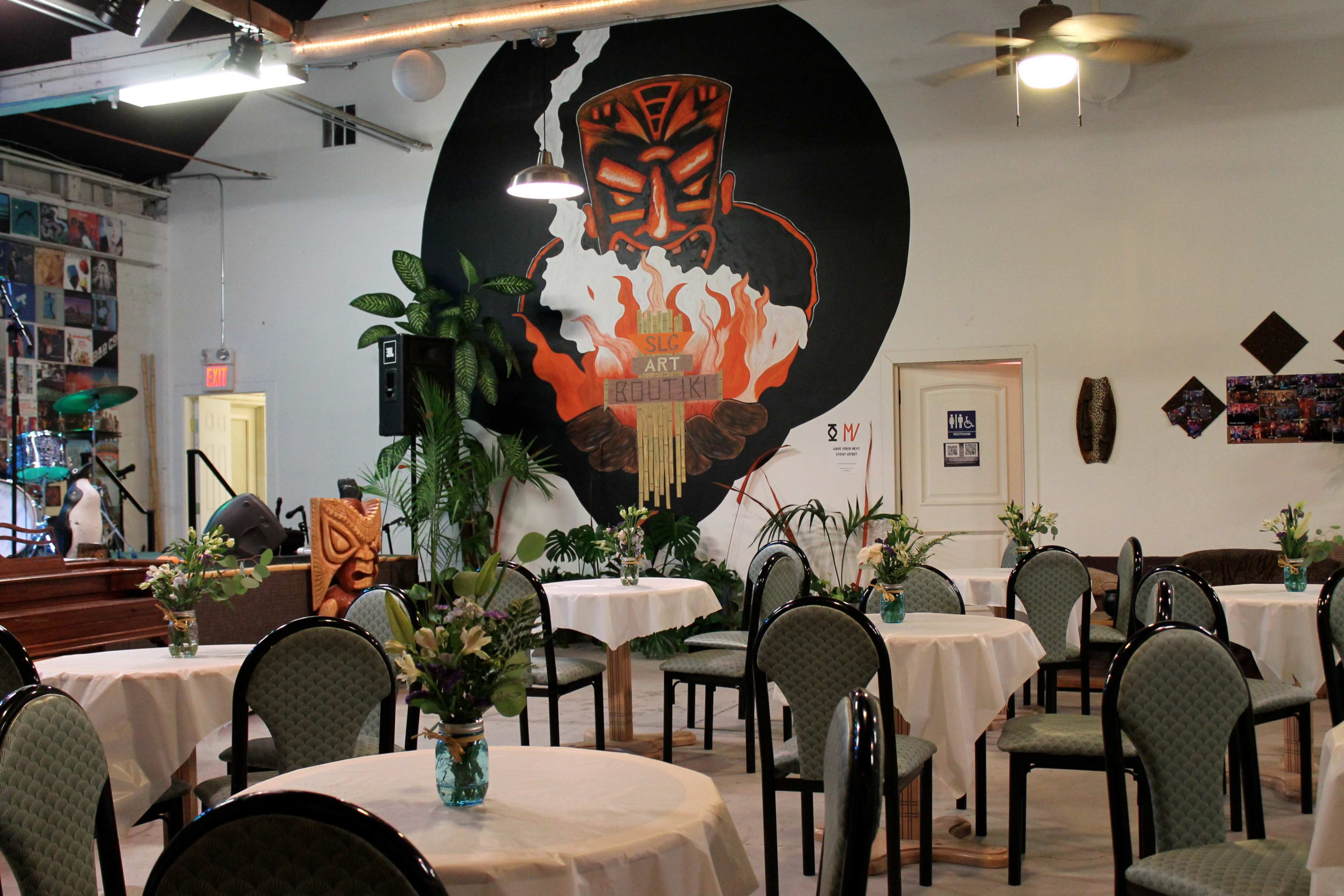 A decorated event space with tables set for dining, featuring a large mural of a Tiki figure on the wall.