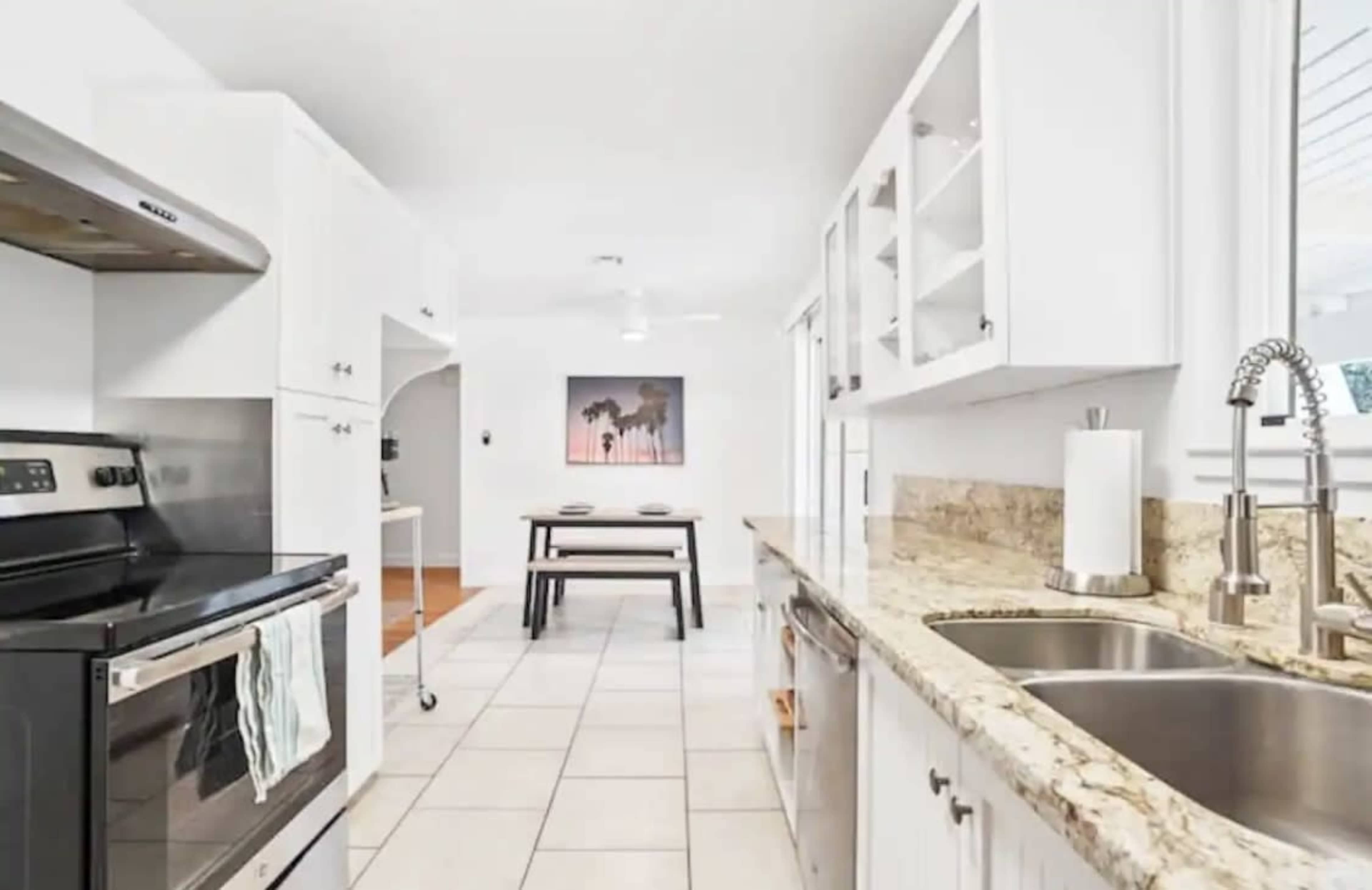A modern kitchen with granite countertops, stainless steel appliances, and white cabinetry, leading to a dining area.