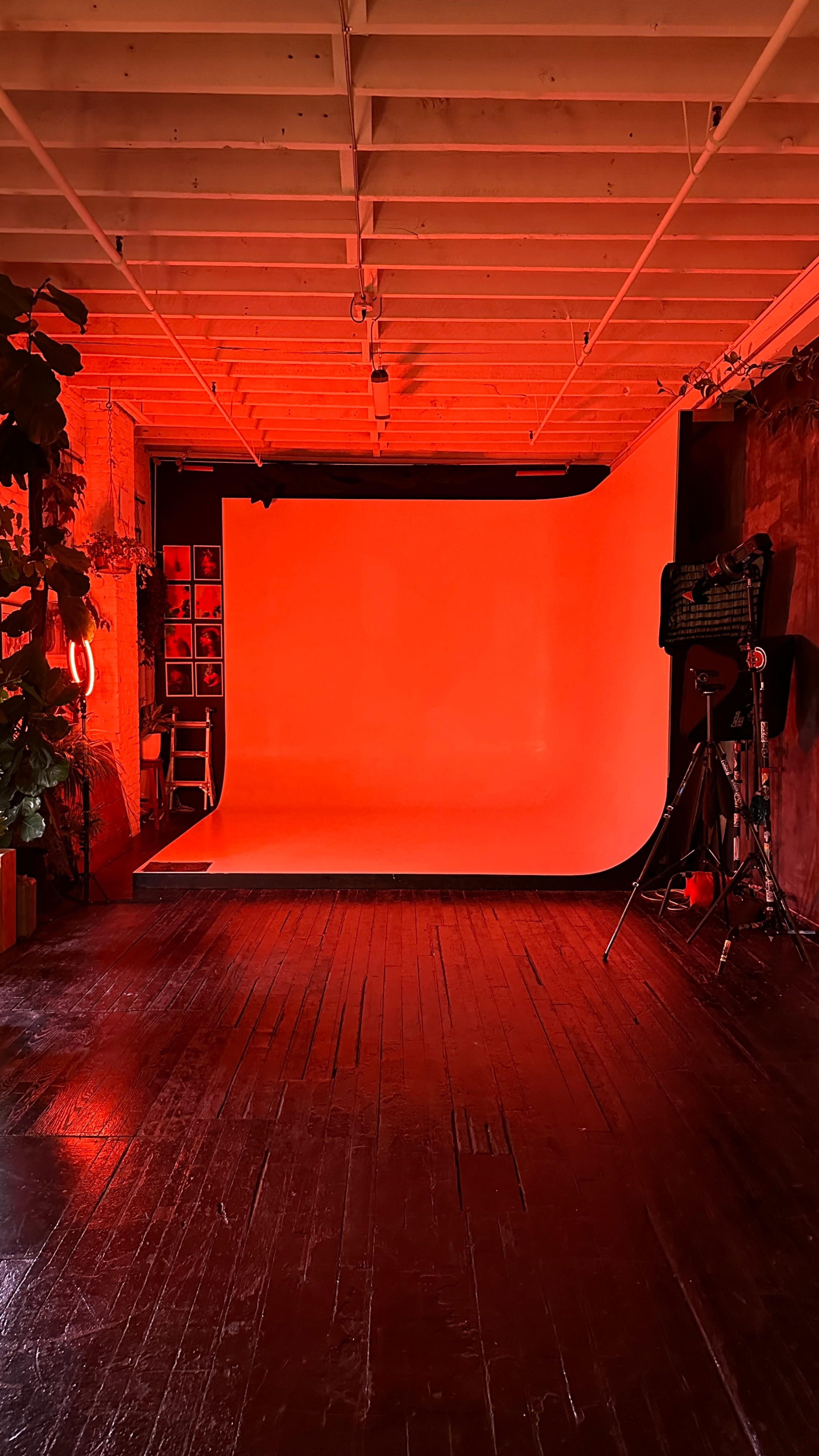 A photography studio with a red-lit backdrop, a white seamless backdrop, and various equipment positioned around the space.