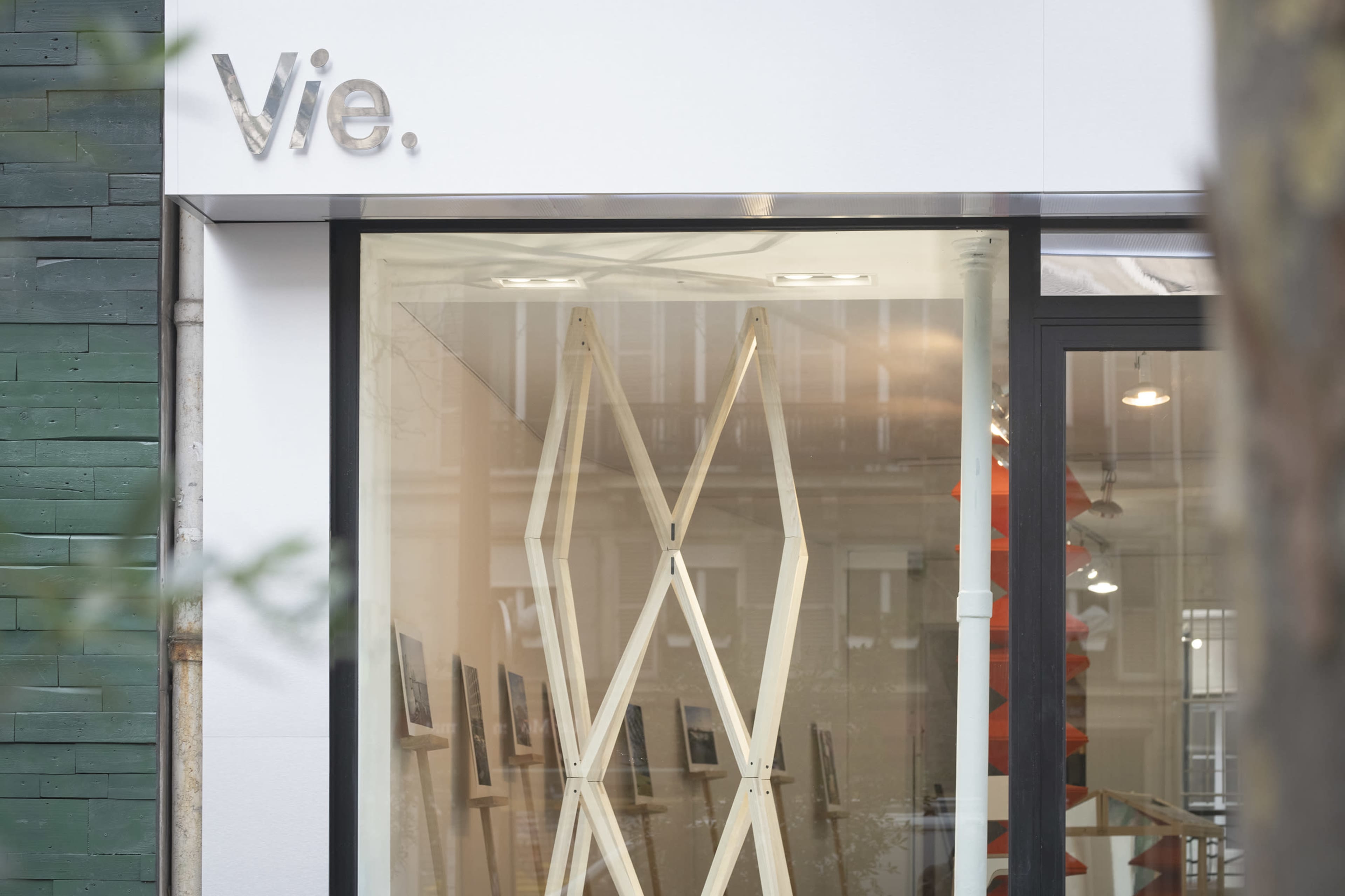 The image shows a storefront with the name "Vie" displayed above a glass entrance, revealing wooden display stands inside.