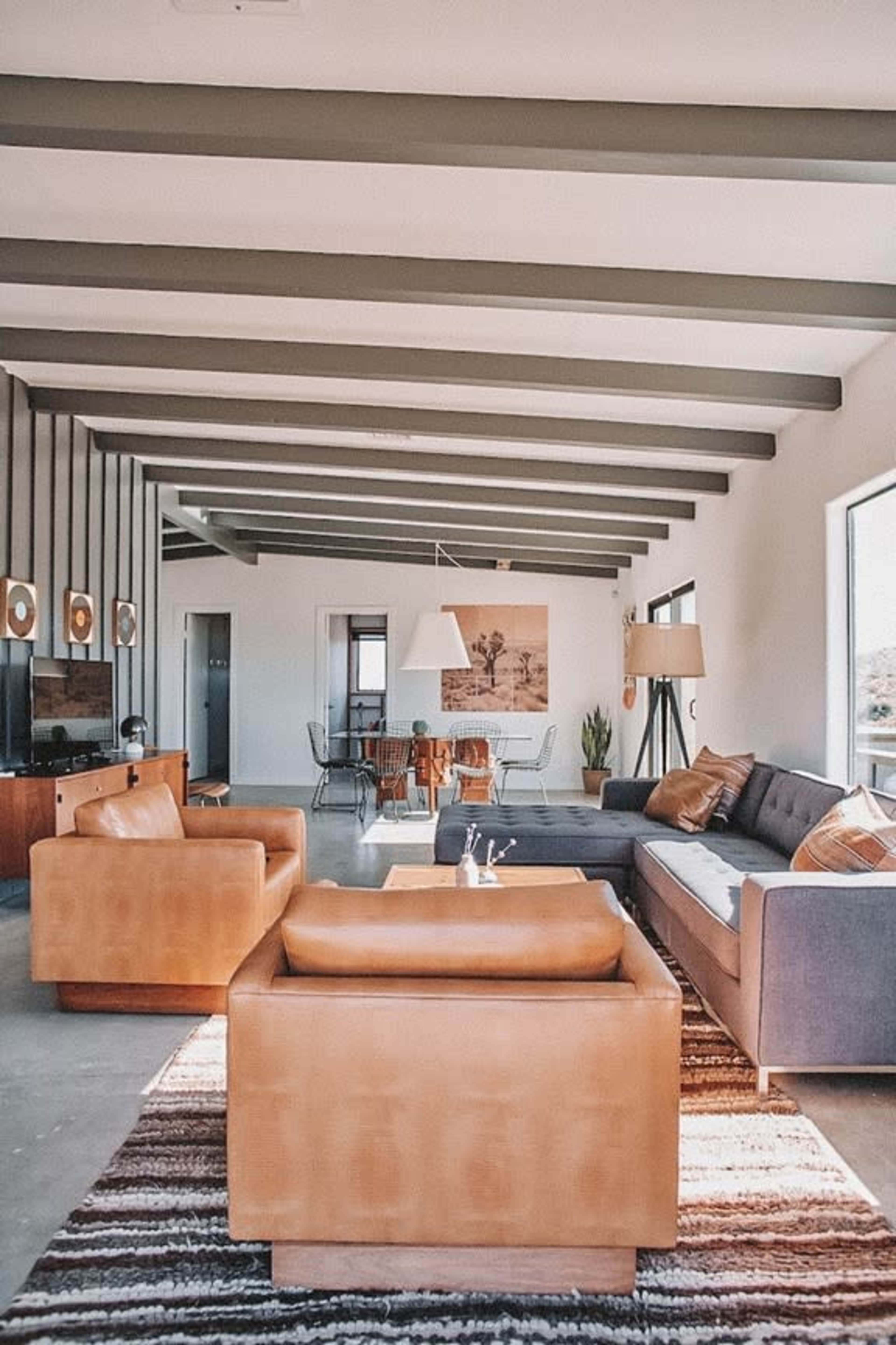 A modern living room with leather furniture, exposed beam ceilings, and a dining area in the background.