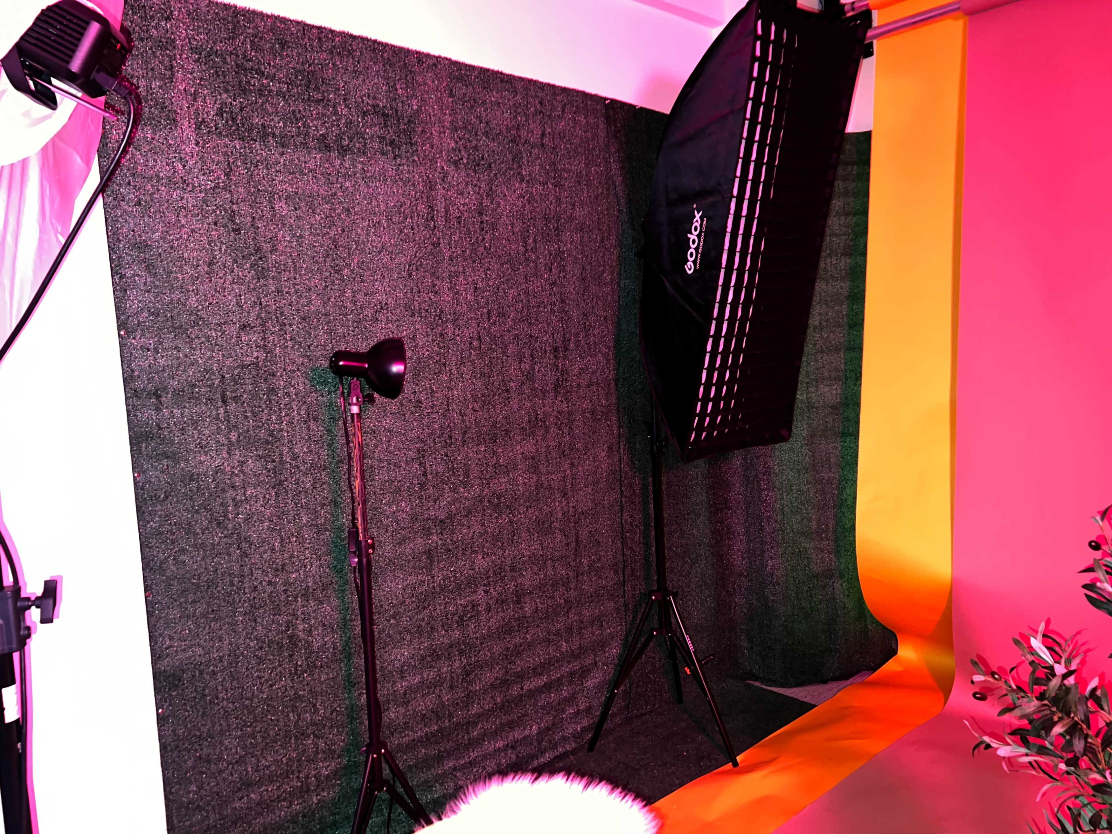 The image shows a photography studio setup with a green backdrop, a softbox light on a stand, and a light with a stand beside it.