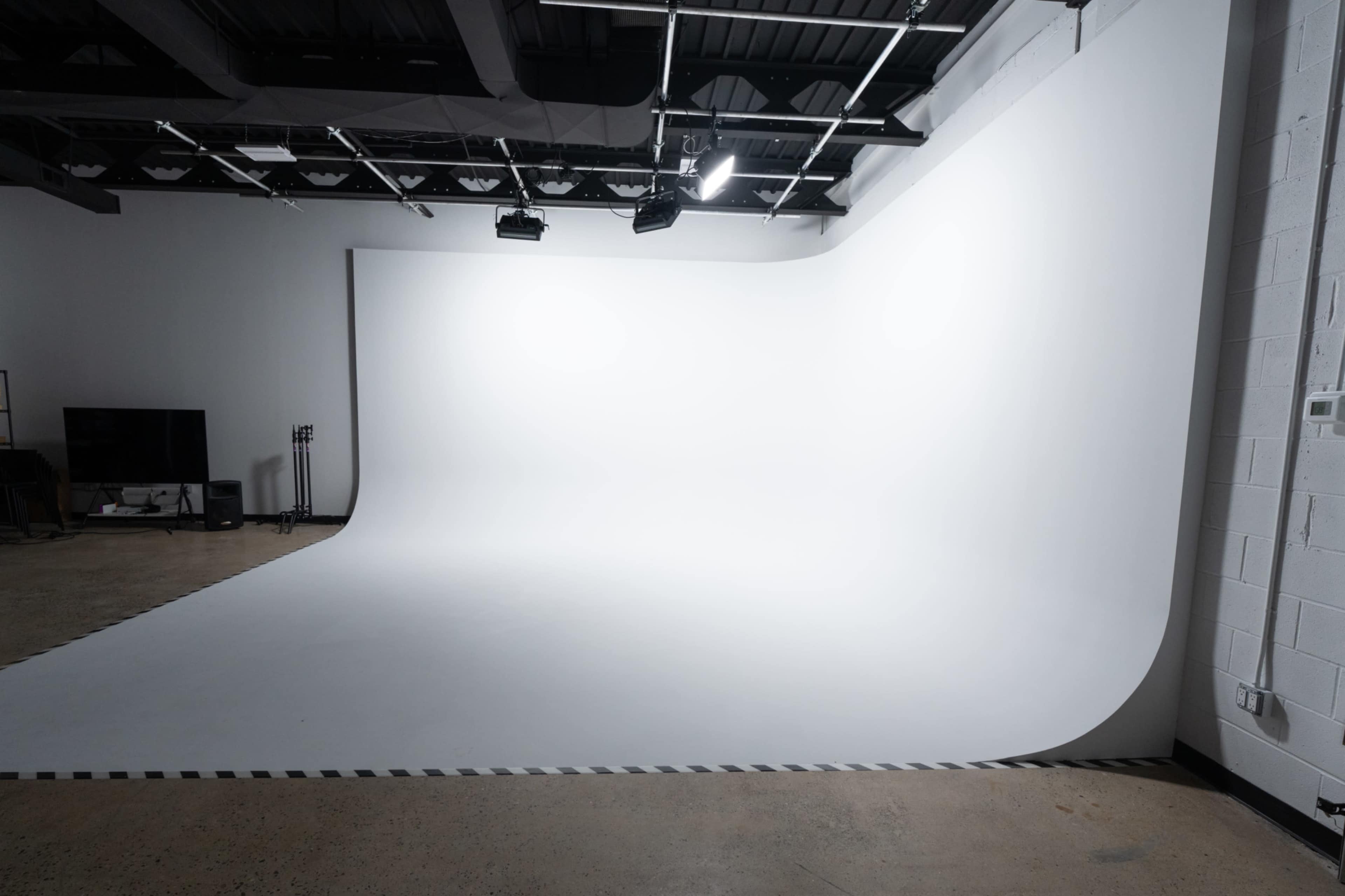 The image depicts a spacious photo studio featuring a seamless white backdrop and a smooth floor surface.