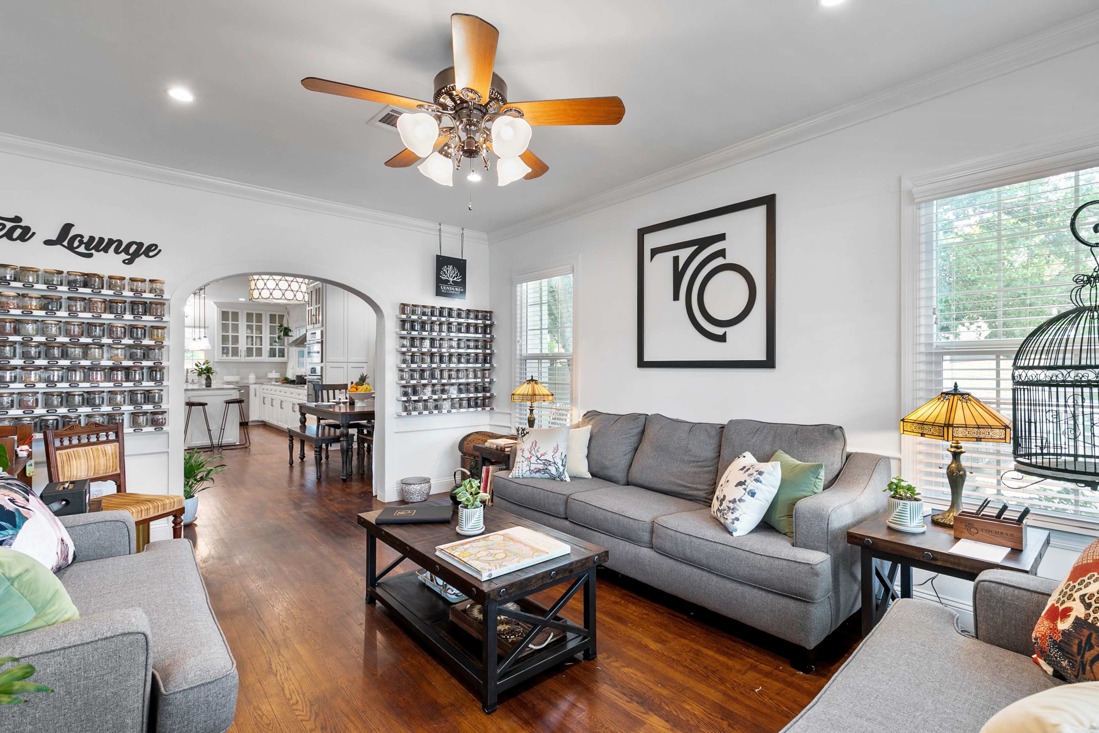 A living room with a ceiling fan, light-colored walls, a coffee table, and a view into a dining area with a large archway.