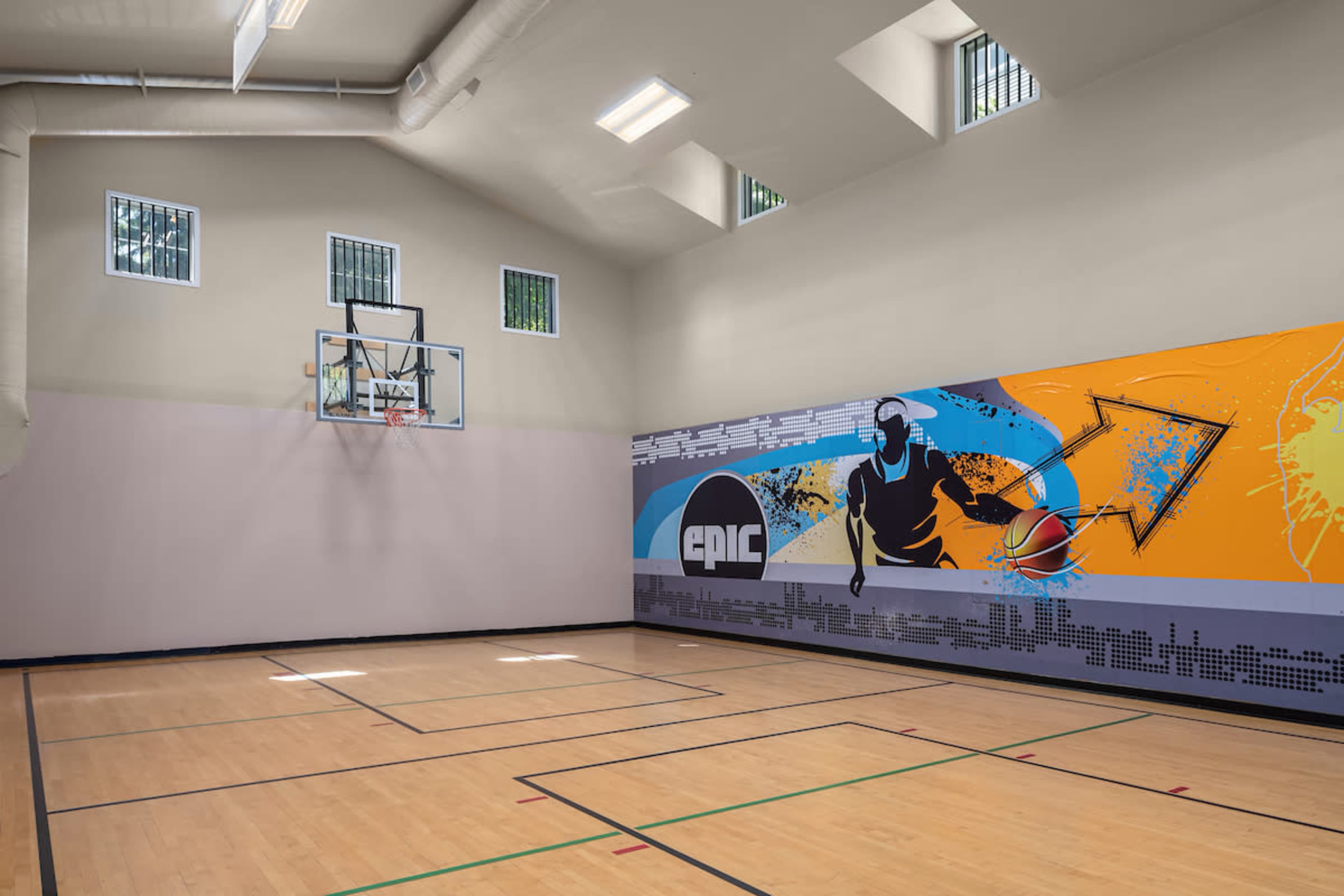 The image shows an indoor basketball court with a hoop, marked floor lines, and a colorful mural featuring a basketball player on one wall.