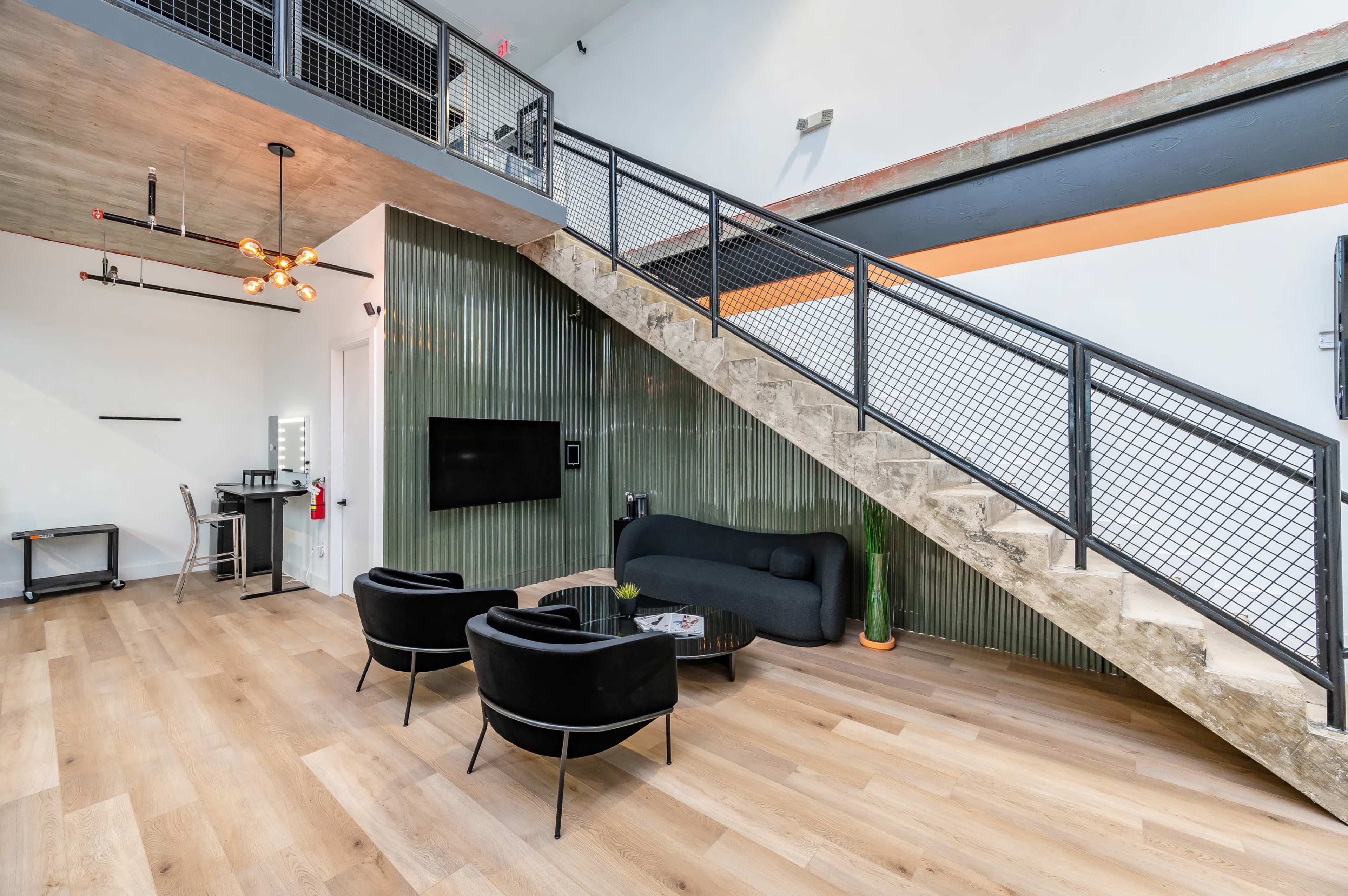 A modern interior space with a staircase, seating area featuring two black chairs and a sofa, and a large wall-mounted TV.