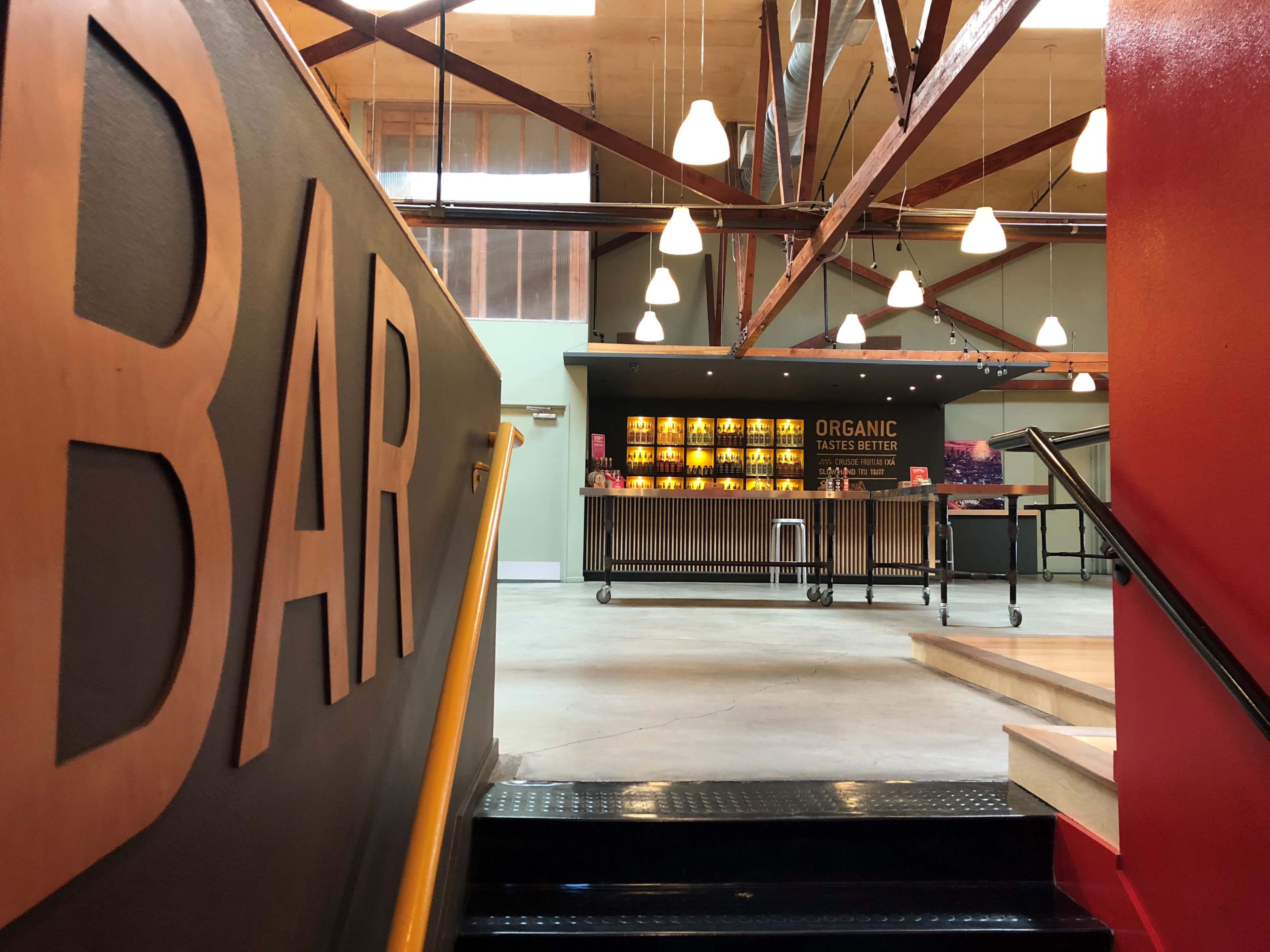 A staircase leads up to a well-lit bar area featuring a wooden counter with shelves displaying organic products.