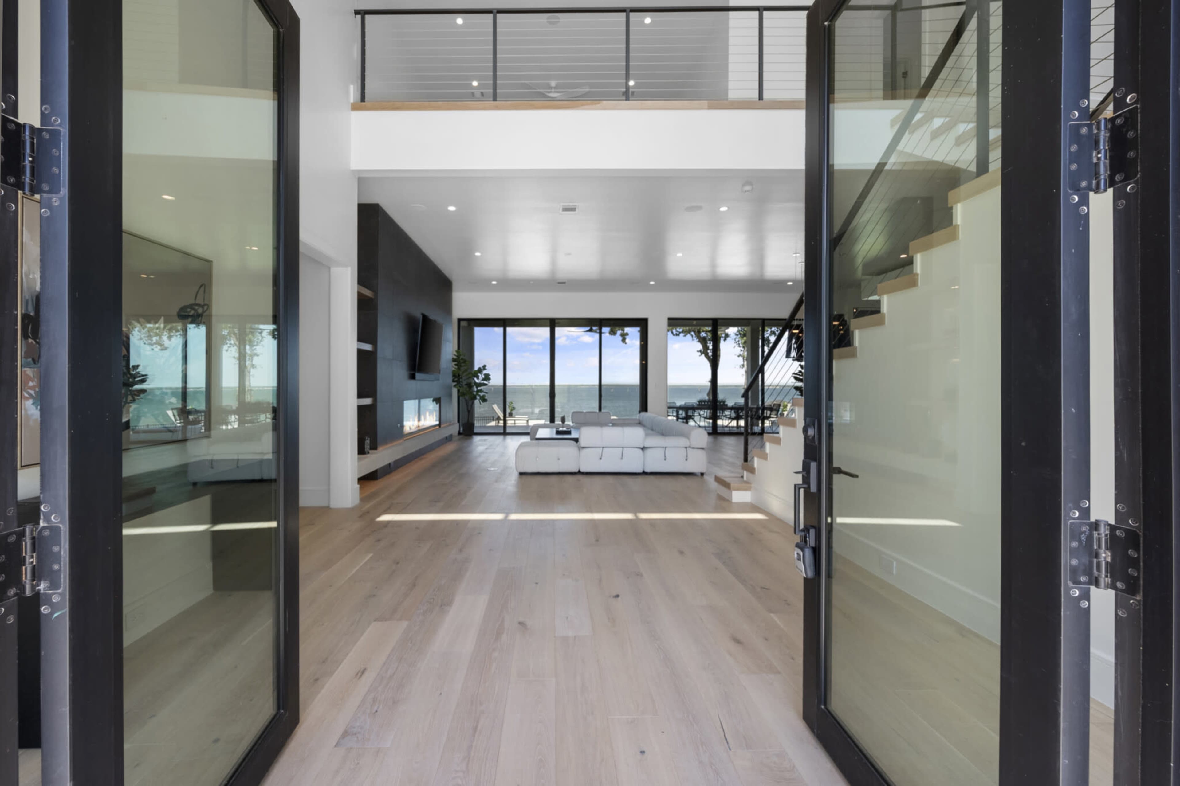 The interior of a modern home with large glass doors opening to a spacious living area that features a white sectional sofa and a view of the ocean through expansive windows.