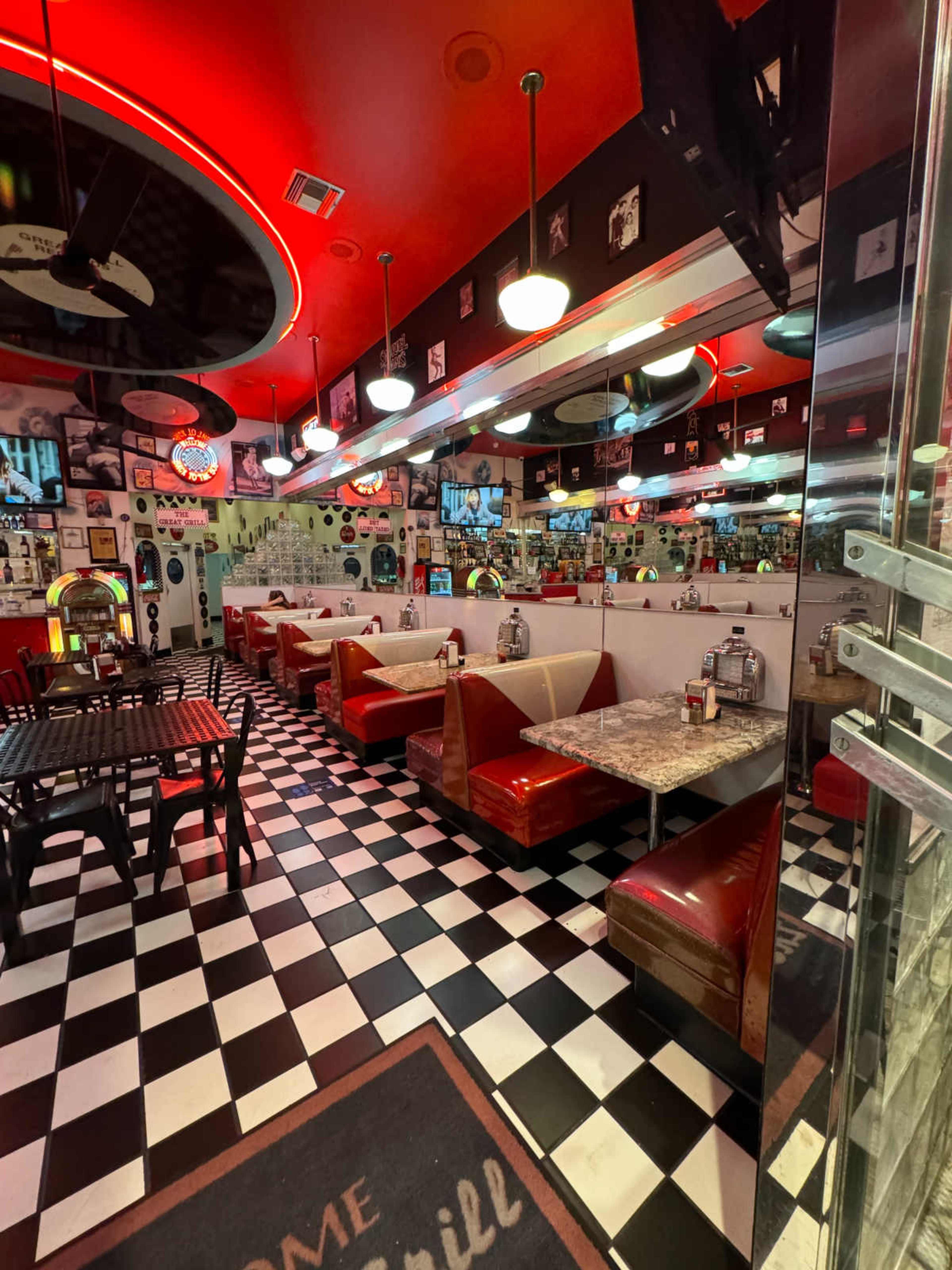 The image shows the interior of a diner with checkered black and white flooring, red booths, and various vintage decorations on the walls.