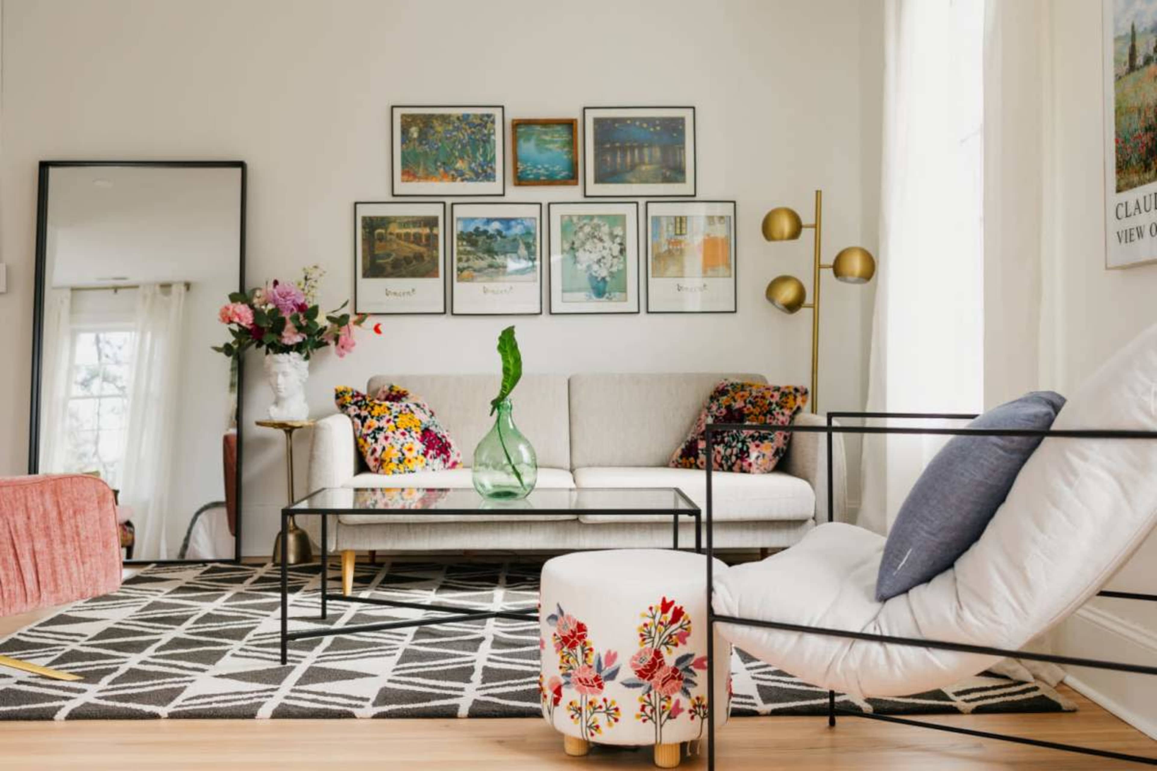 The living room features a light-colored sofa, a glass coffee table, and a gallery wall of framed artwork, with decorative plants and colorful cushions adding contrasting elements.