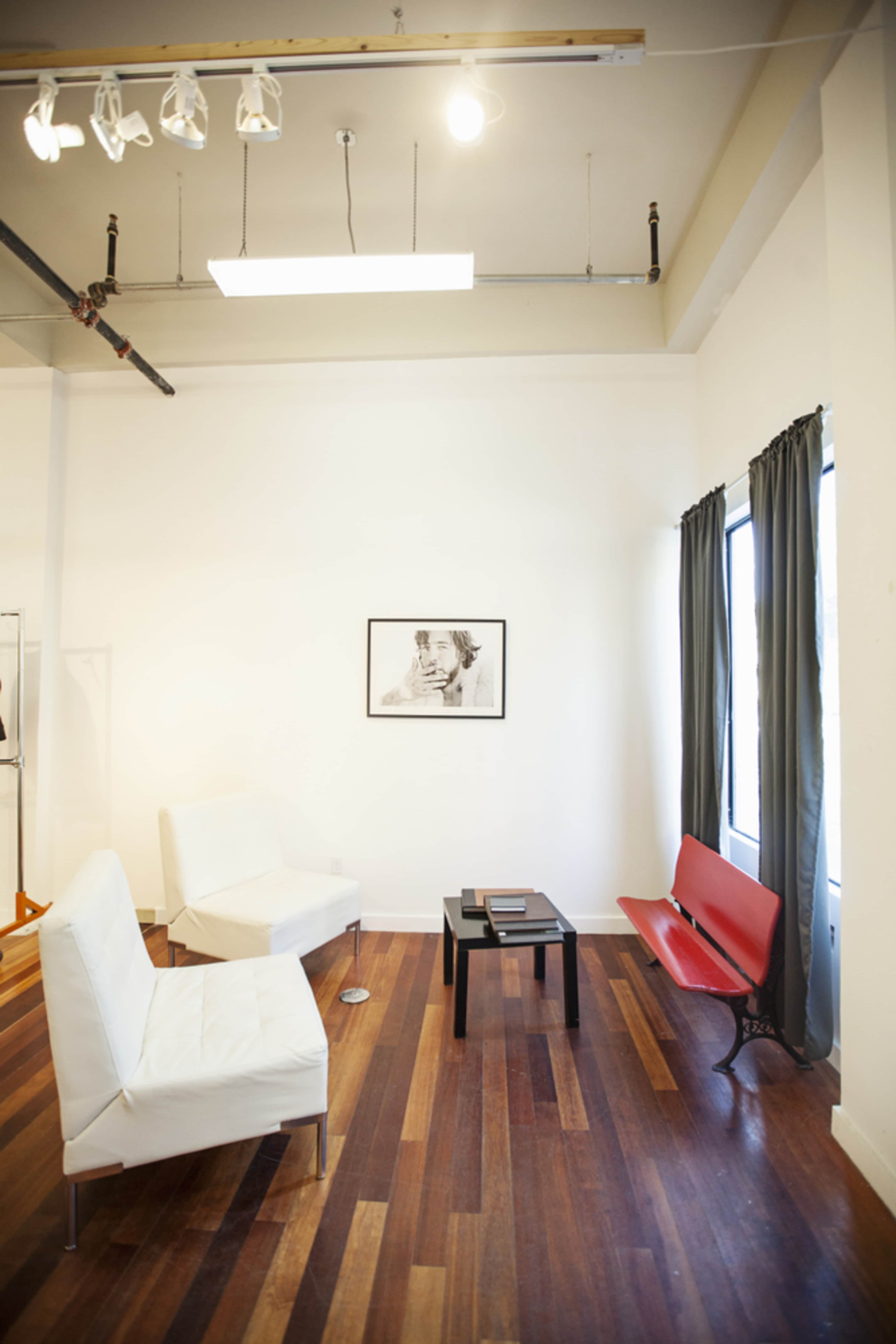 A minimalist interior space with two white chairs, a red bench, a black table, and a framed picture against a white wall.