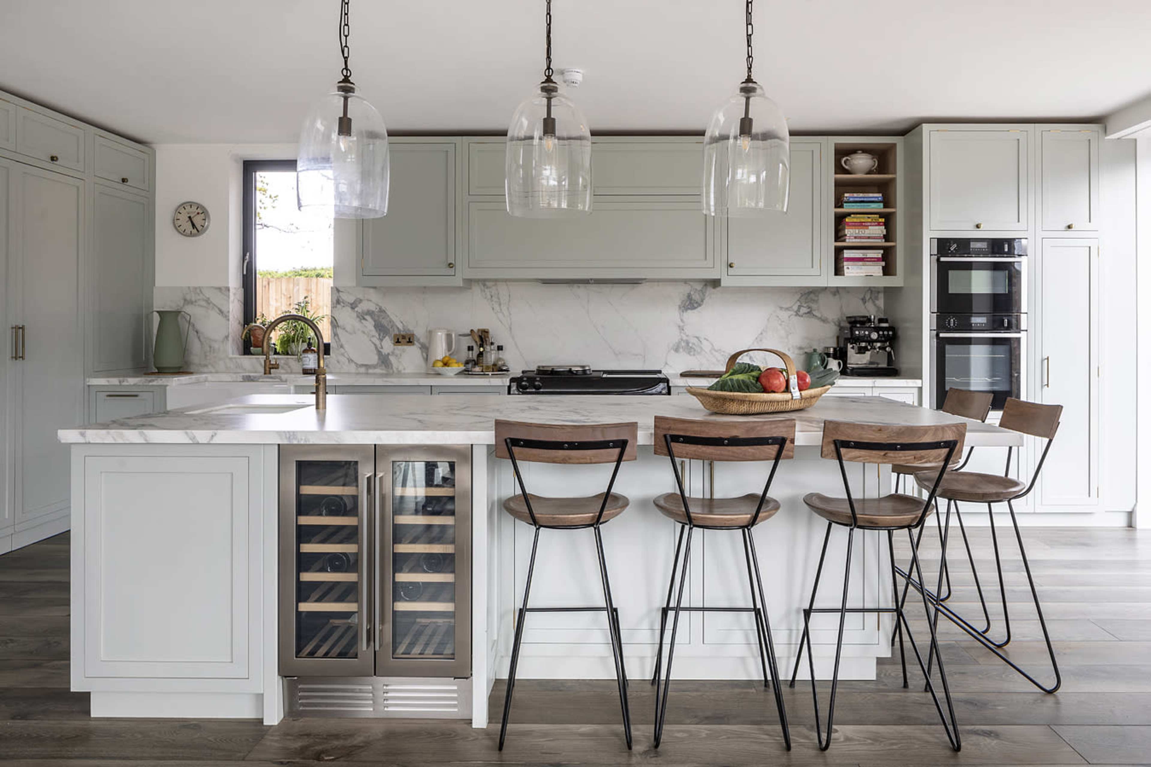 A modern kitchen features a large island with a marble countertop, bar stools, and pendant lighting, alongside cabinets and a stainless steel refrigerator.