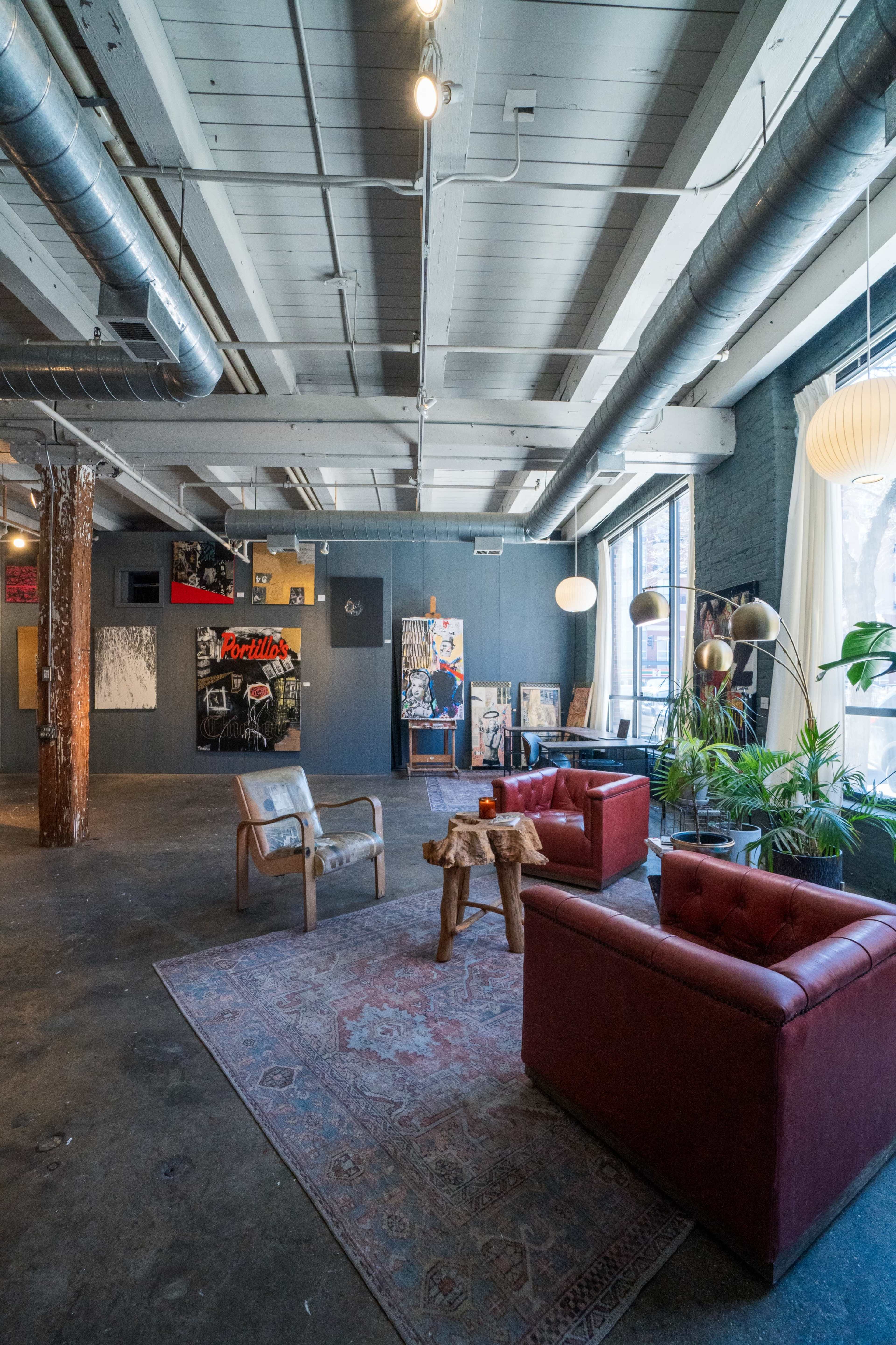 A spacious room with exposed beams, two red leather armchairs, a wooden side table, and various artworks displayed on the walls.