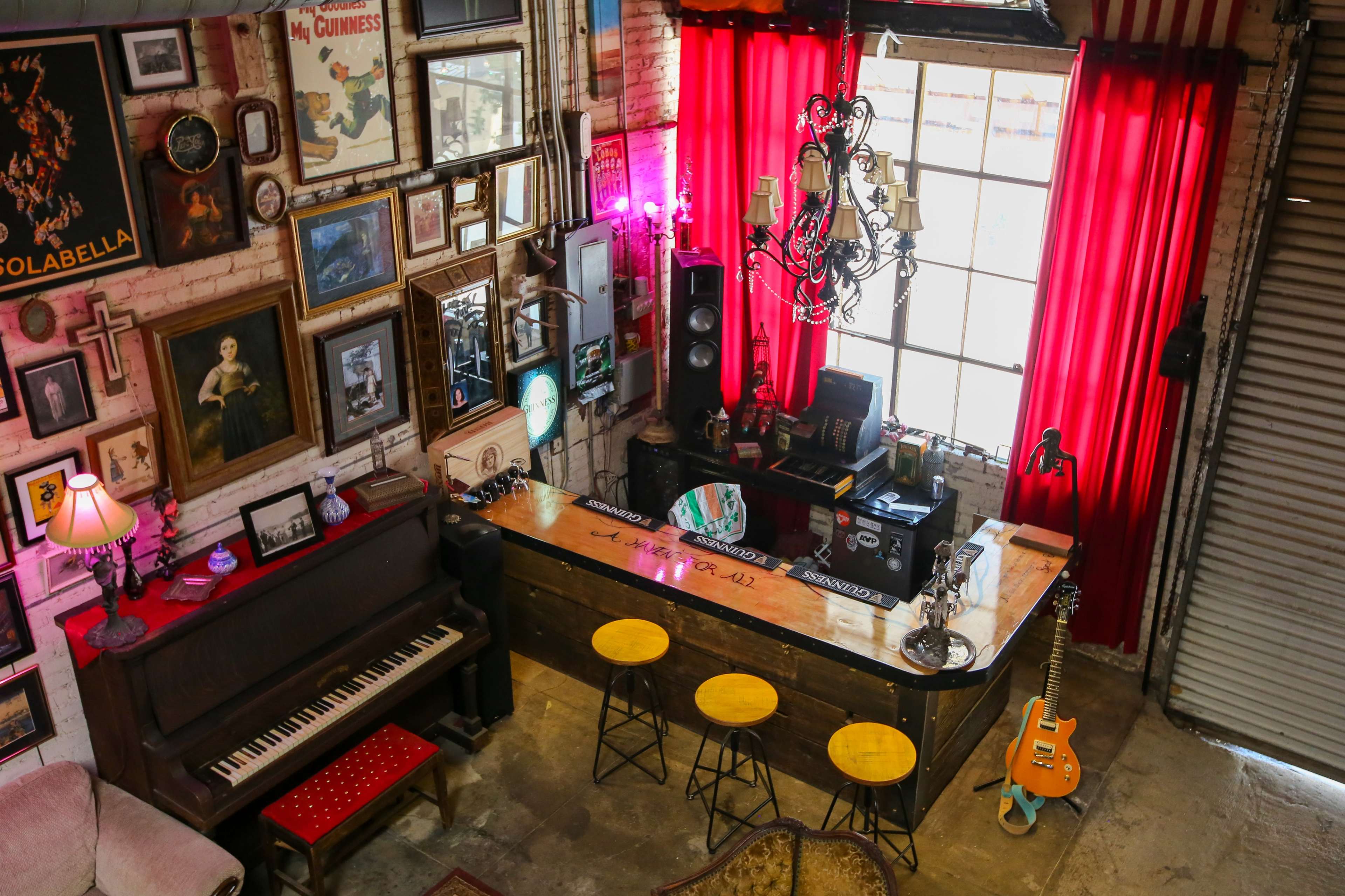 The image shows a cozy bar area with a piano, vintage decor on the walls, and a large window draped in red curtains.