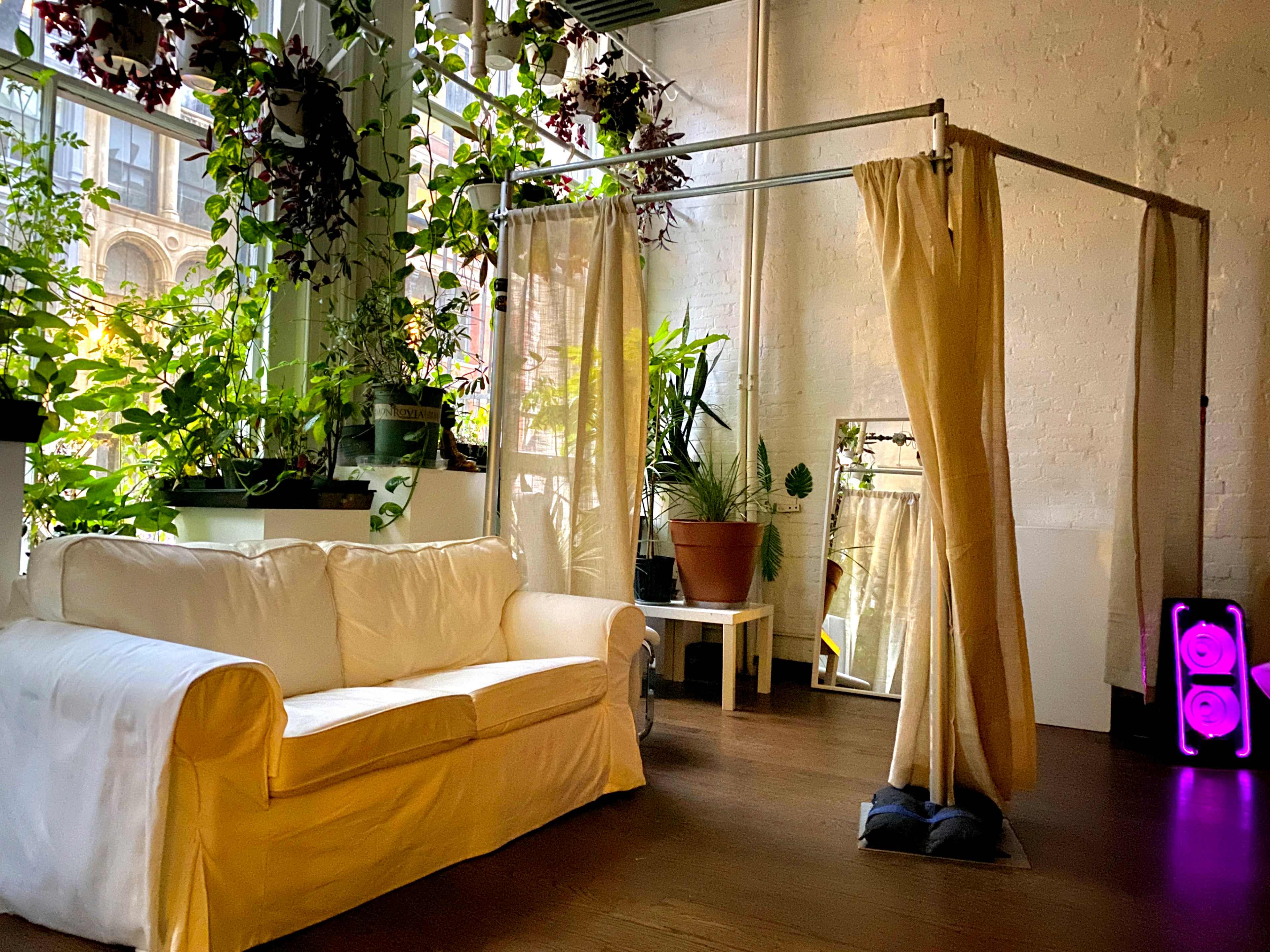 A bright interior space featuring a white sofa, potted plants, and a curtain divider.