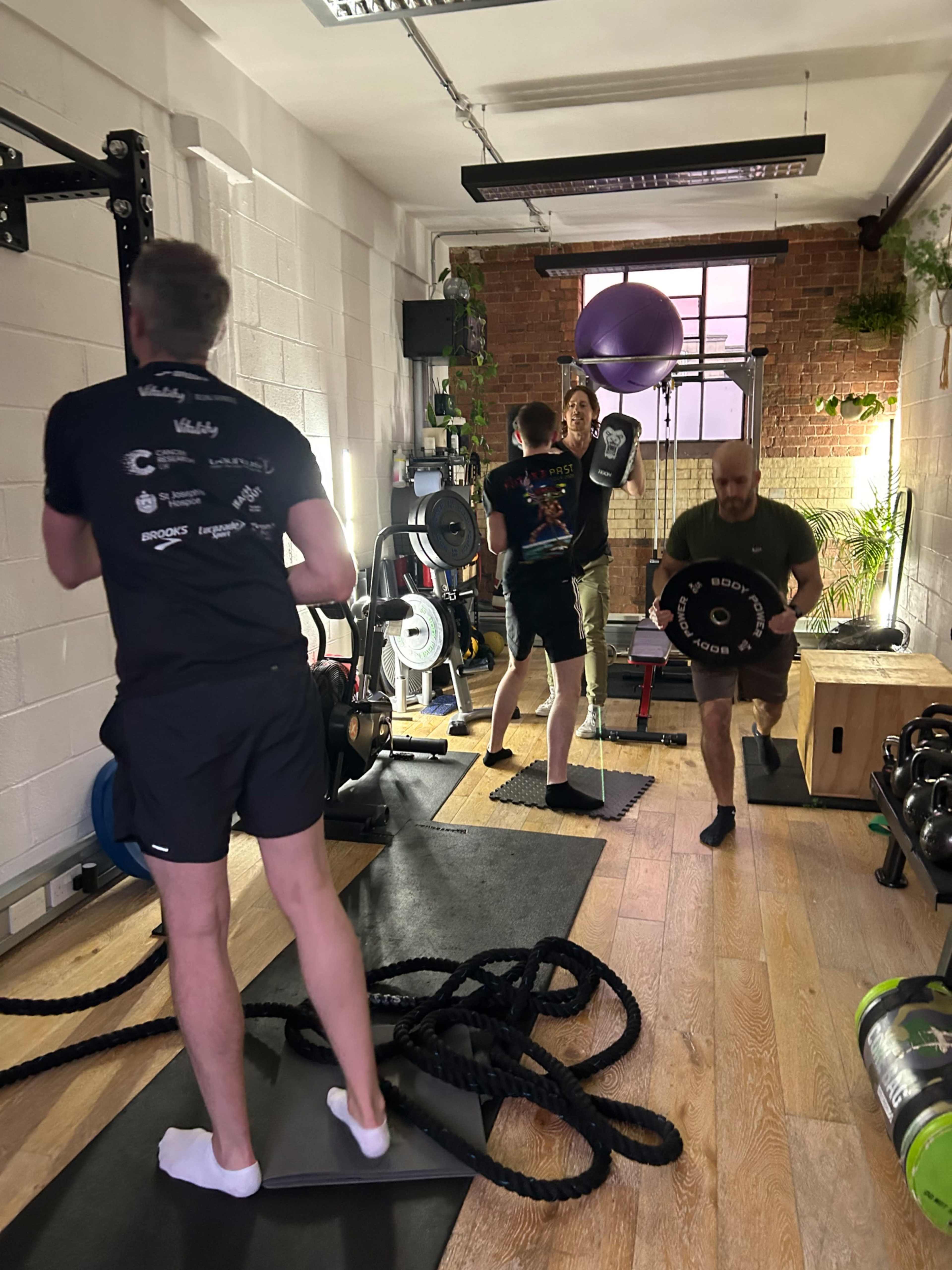 Three individuals are engaged in a workout session in a gym, utilizing weights and ropes amidst a variety of fitness equipment.