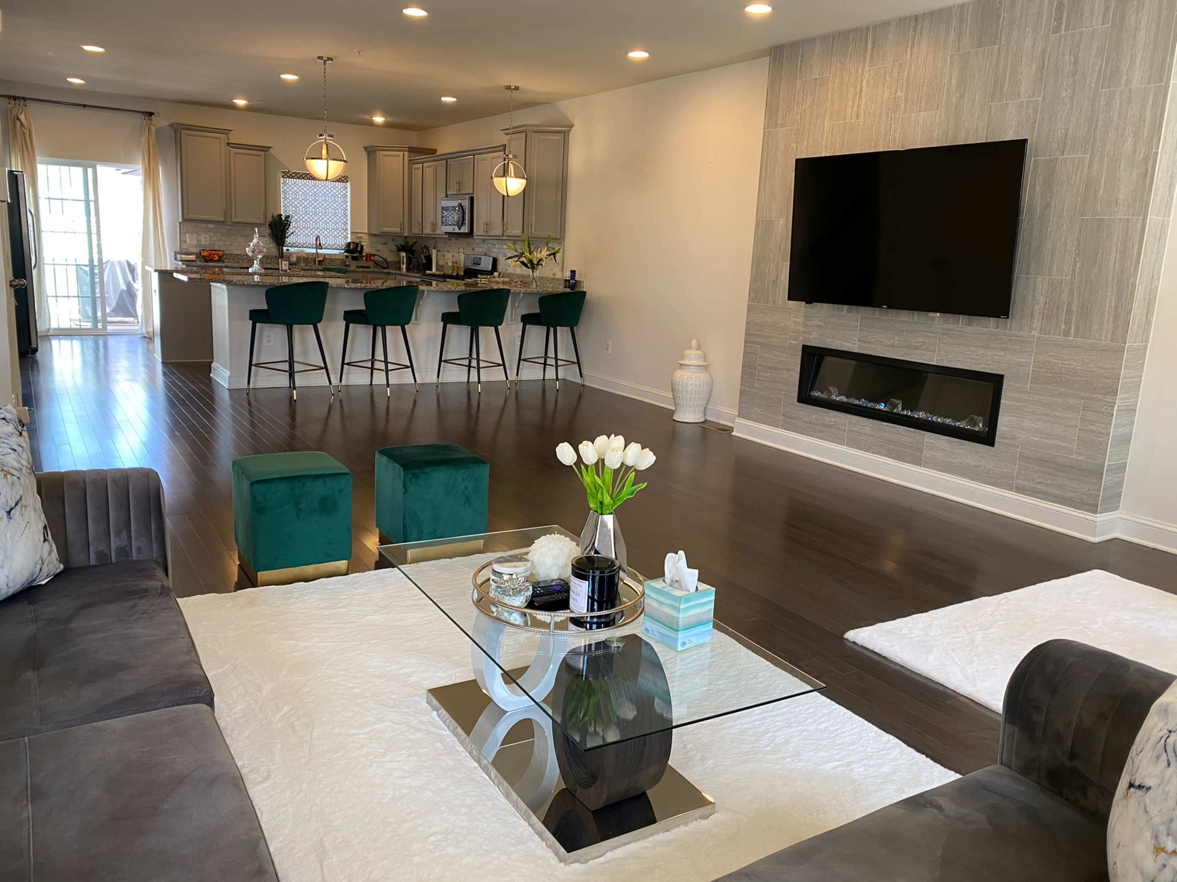 A modern living room with a glass coffee table and a sectional sofa, leading to an open-concept kitchen with bar seating.
