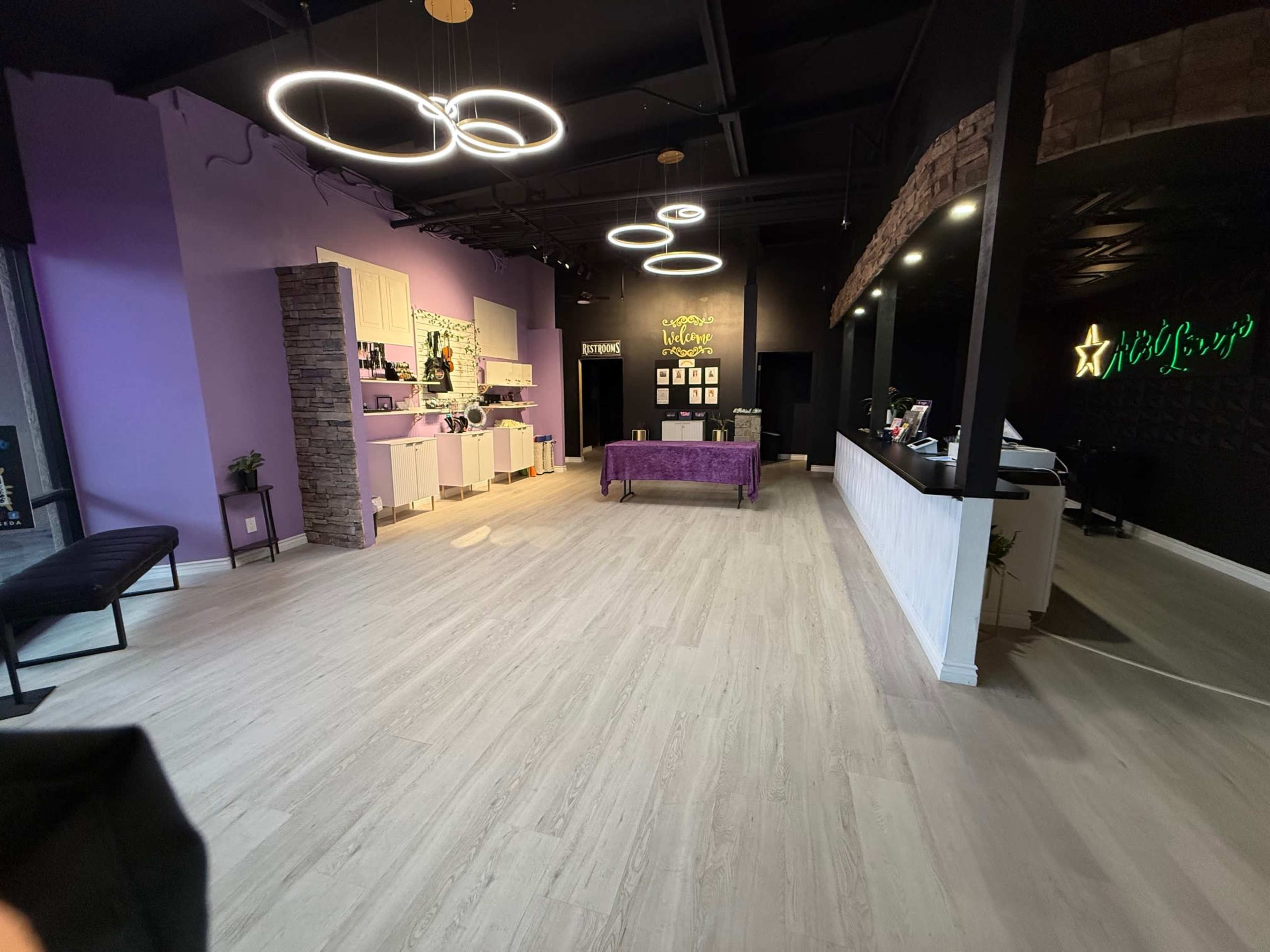 The image shows an interior space featuring purple walls, modern lighting fixtures, a reception area with a white counter, and a central seating area with a purple couch.