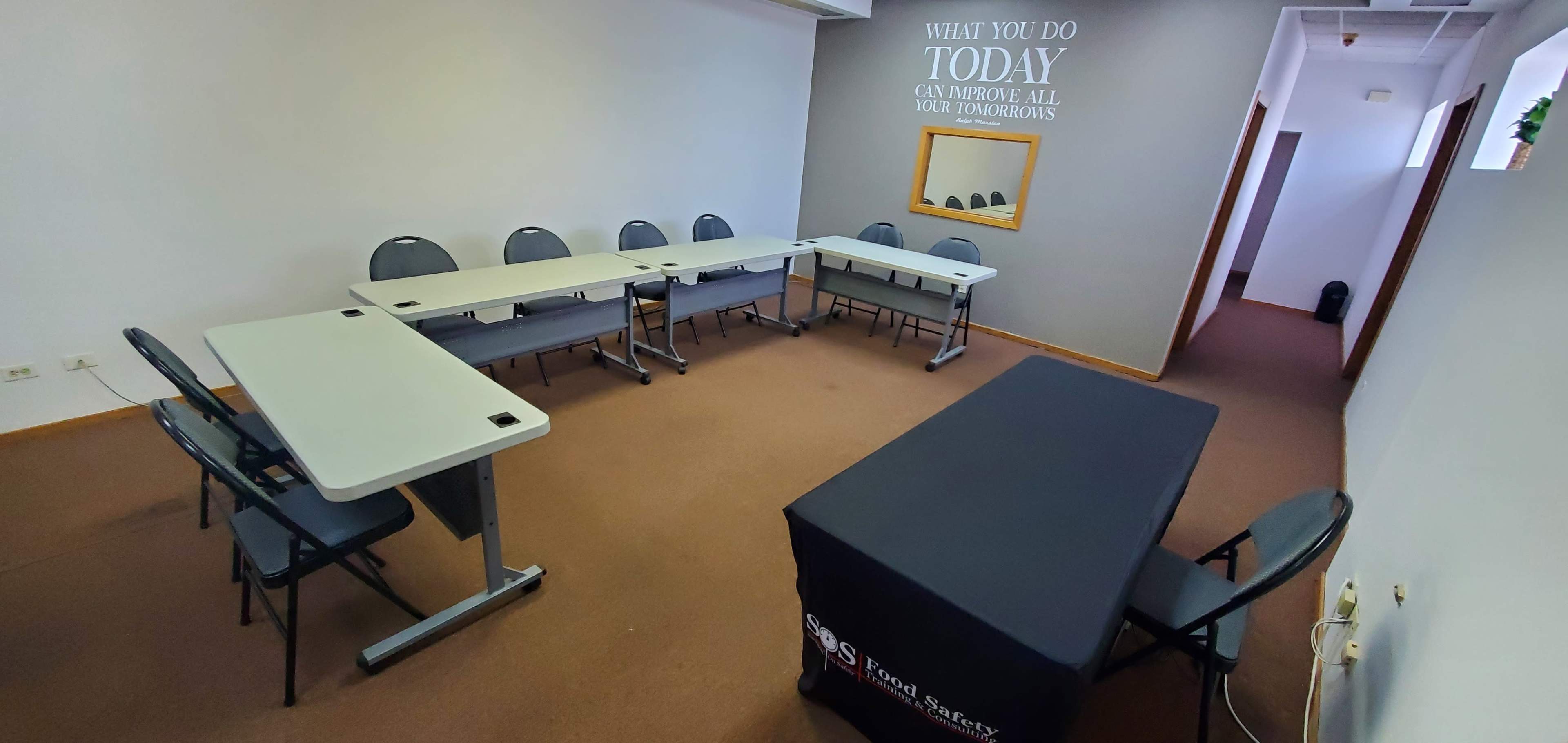 A small meeting room features a U-shaped arrangement of tables and chairs, with a table covered by a black cloth in the foreground.