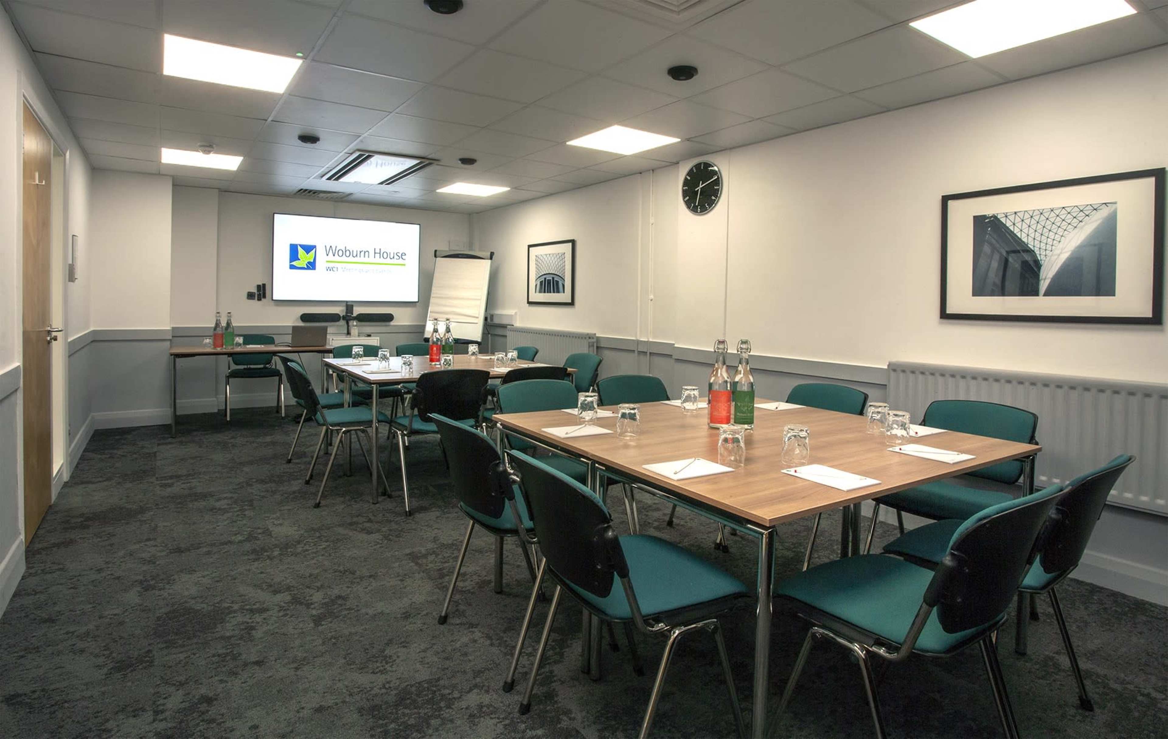A conference room is set up with multiple tables, chairs, a presentation screen, and water bottles arranged neatly.