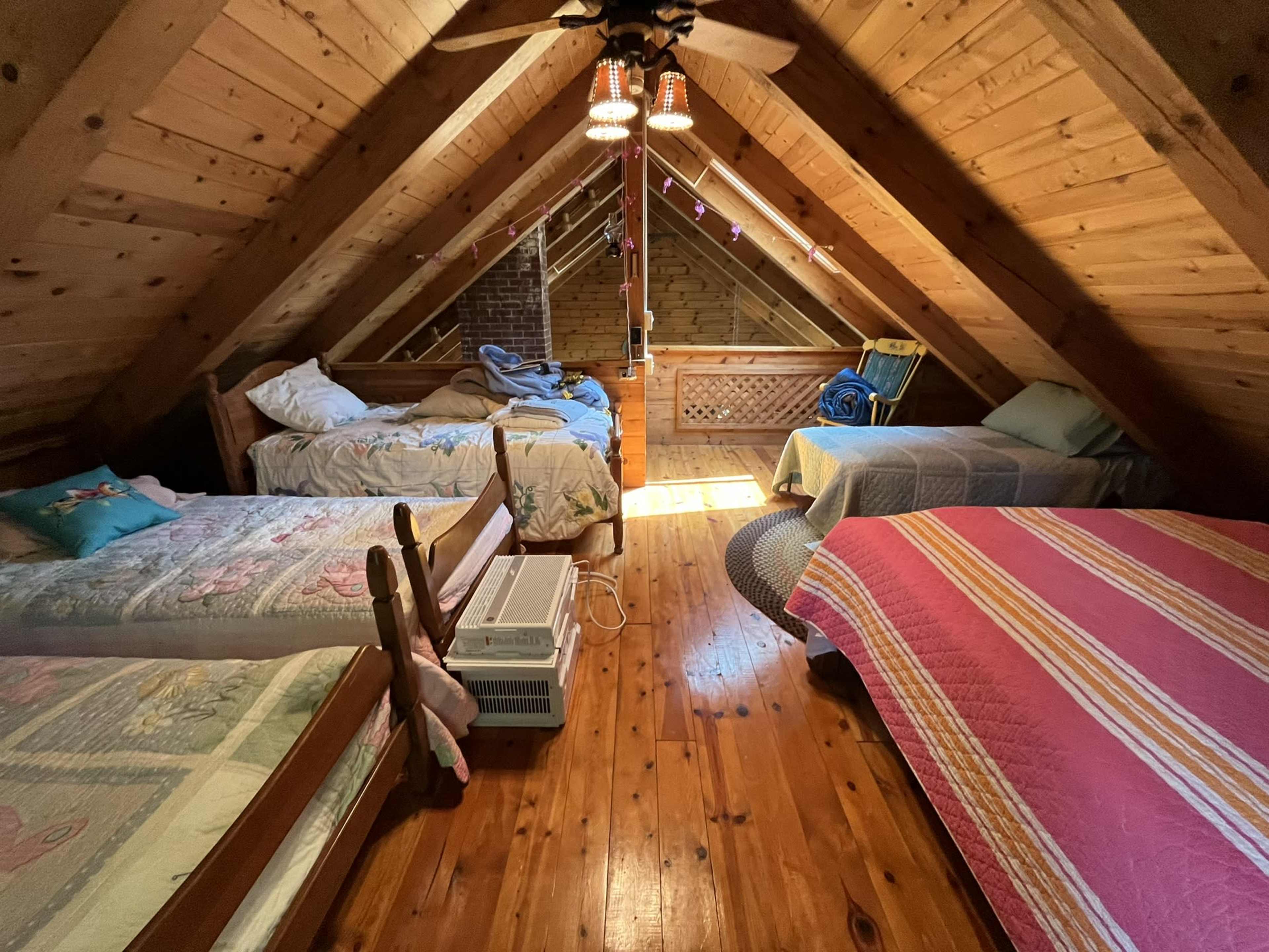 A wooden attic room with three beds arranged on a polished wooden floor beneath sloped, exposed beams.
