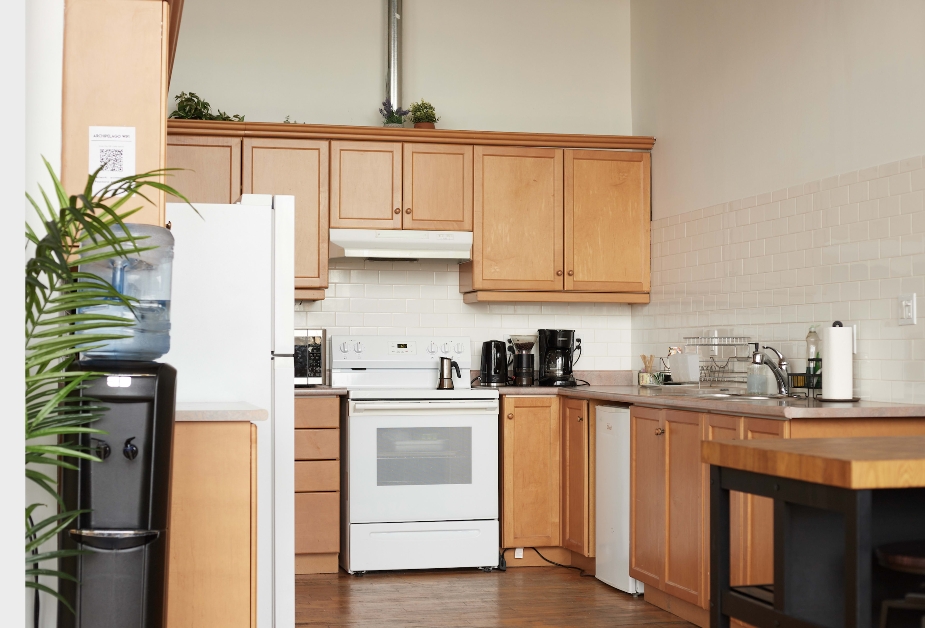 The image shows a modern kitchen with wooden cabinets, a white stove, and various appliances including a coffee maker and a refrigerator.
