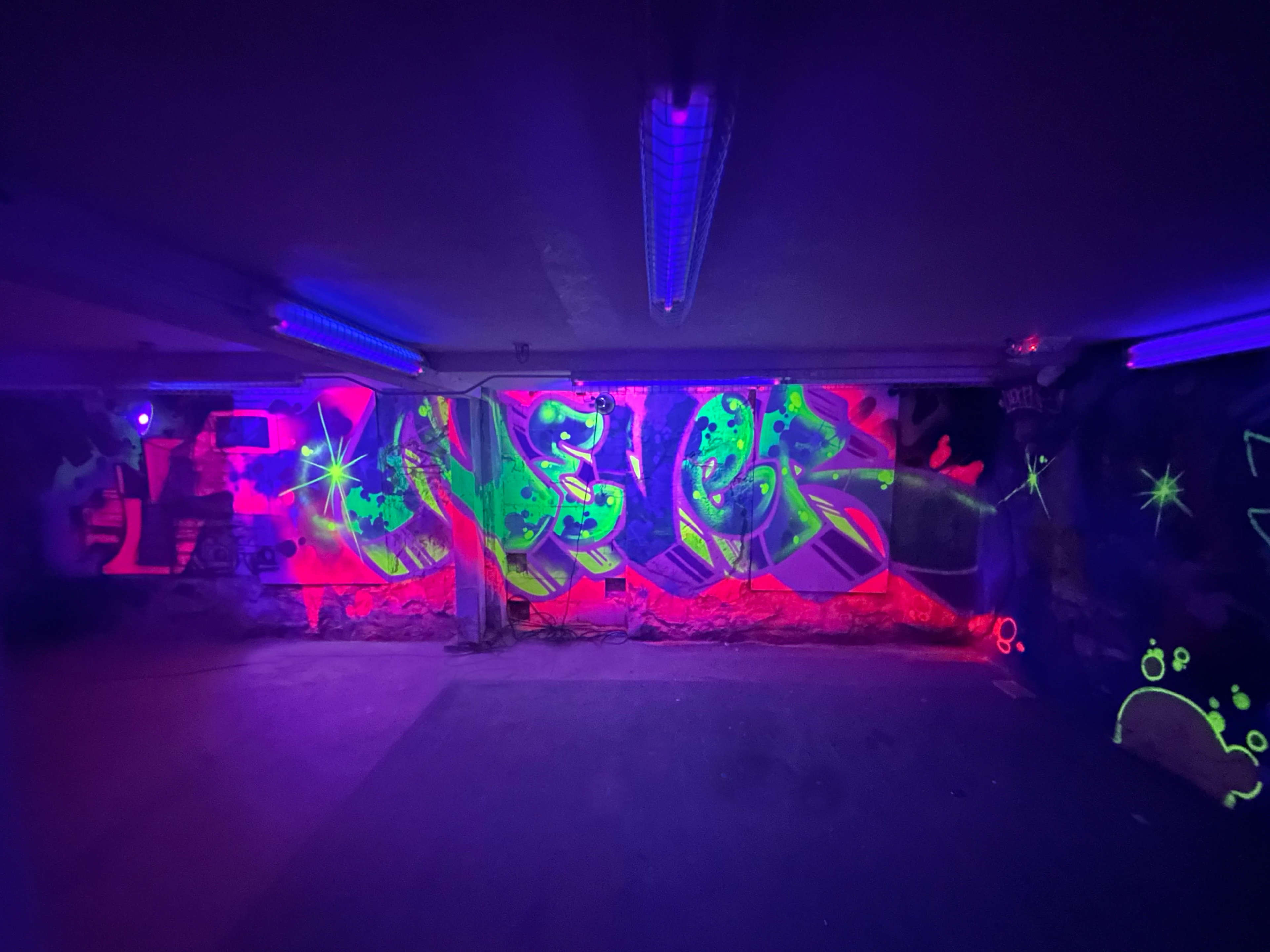 Vibrant graffiti art illuminated by ultraviolet lights in a dimly lit indoor space.