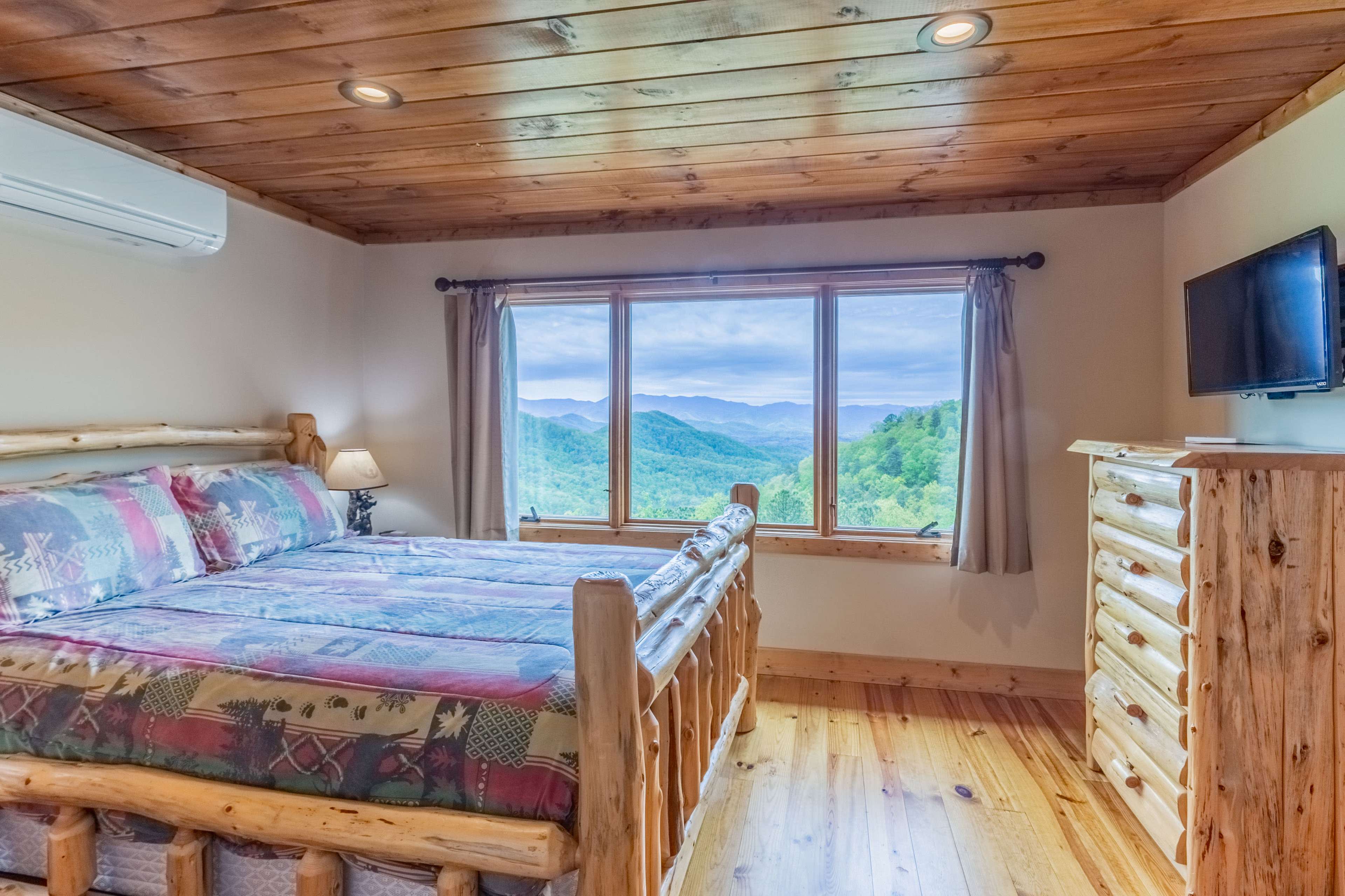 A cozy bedroom featuring a log-style bed, wooden furniture, and a large window with a mountain view.