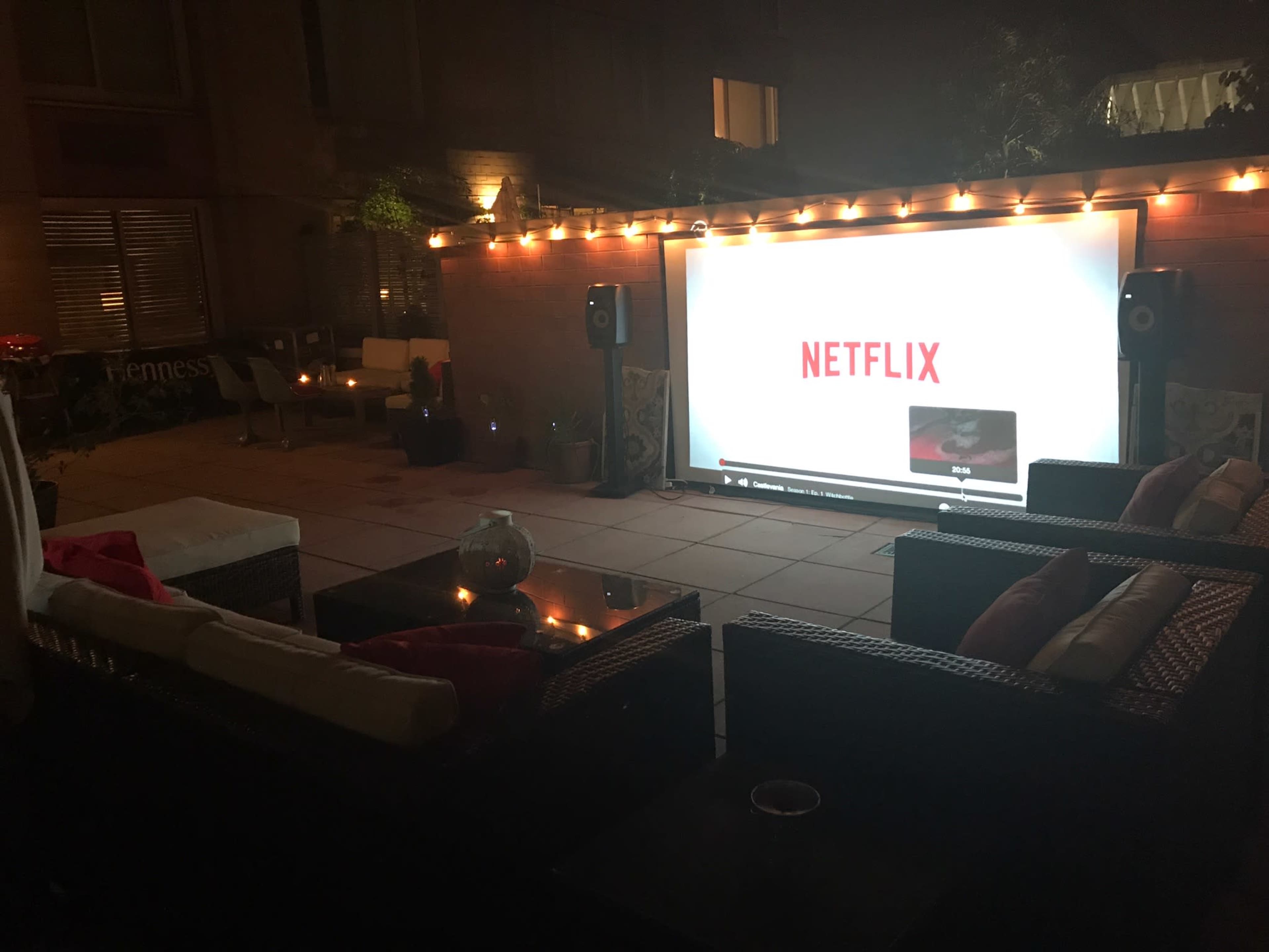 The outdoor space features a large projector screen displaying a Netflix logo, surrounded by comfortable seating and ambient lighting.