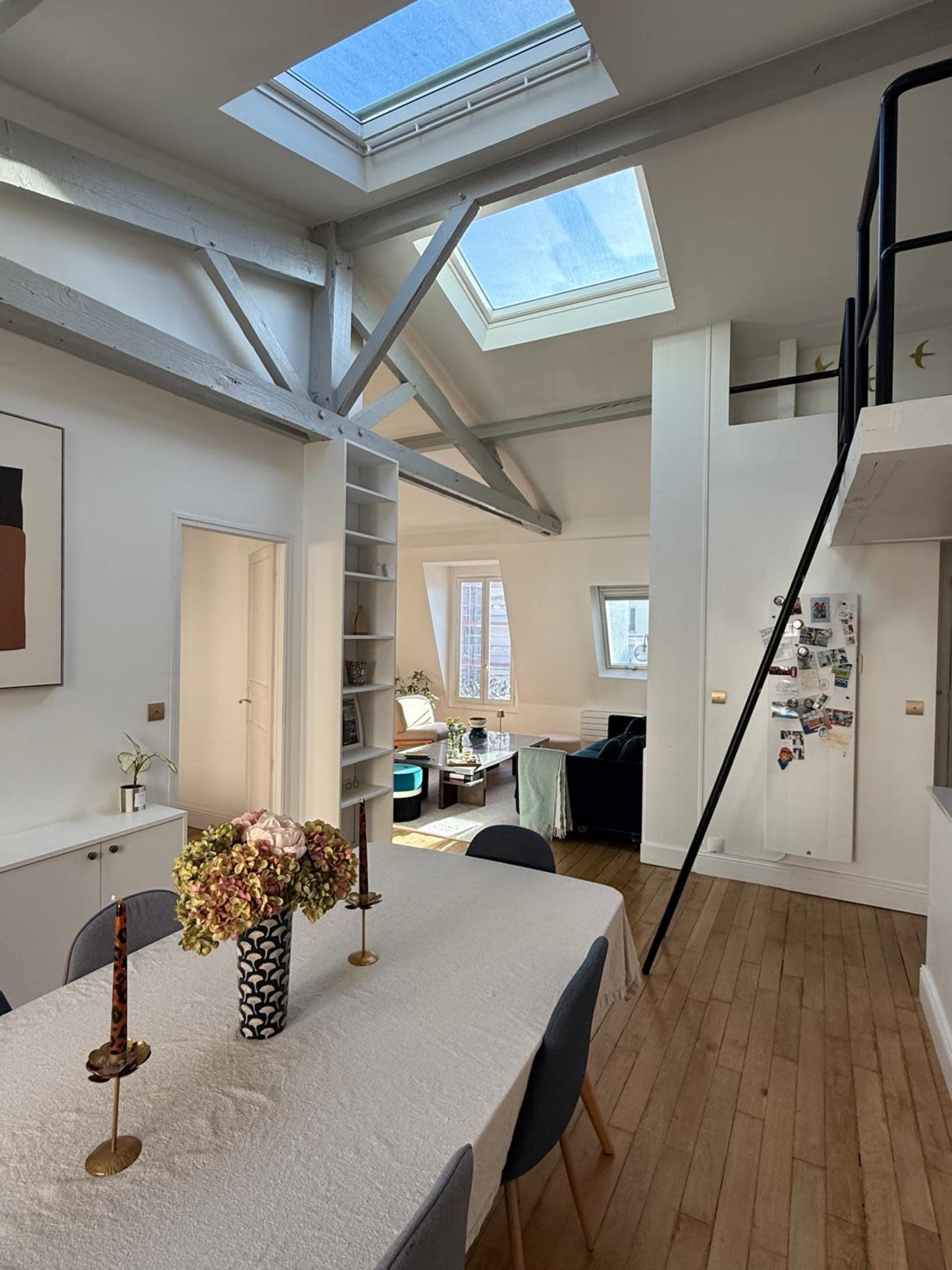The image shows a modern dining area with a table set for six, featuring a skylight overhead, and a living space visible in the background.