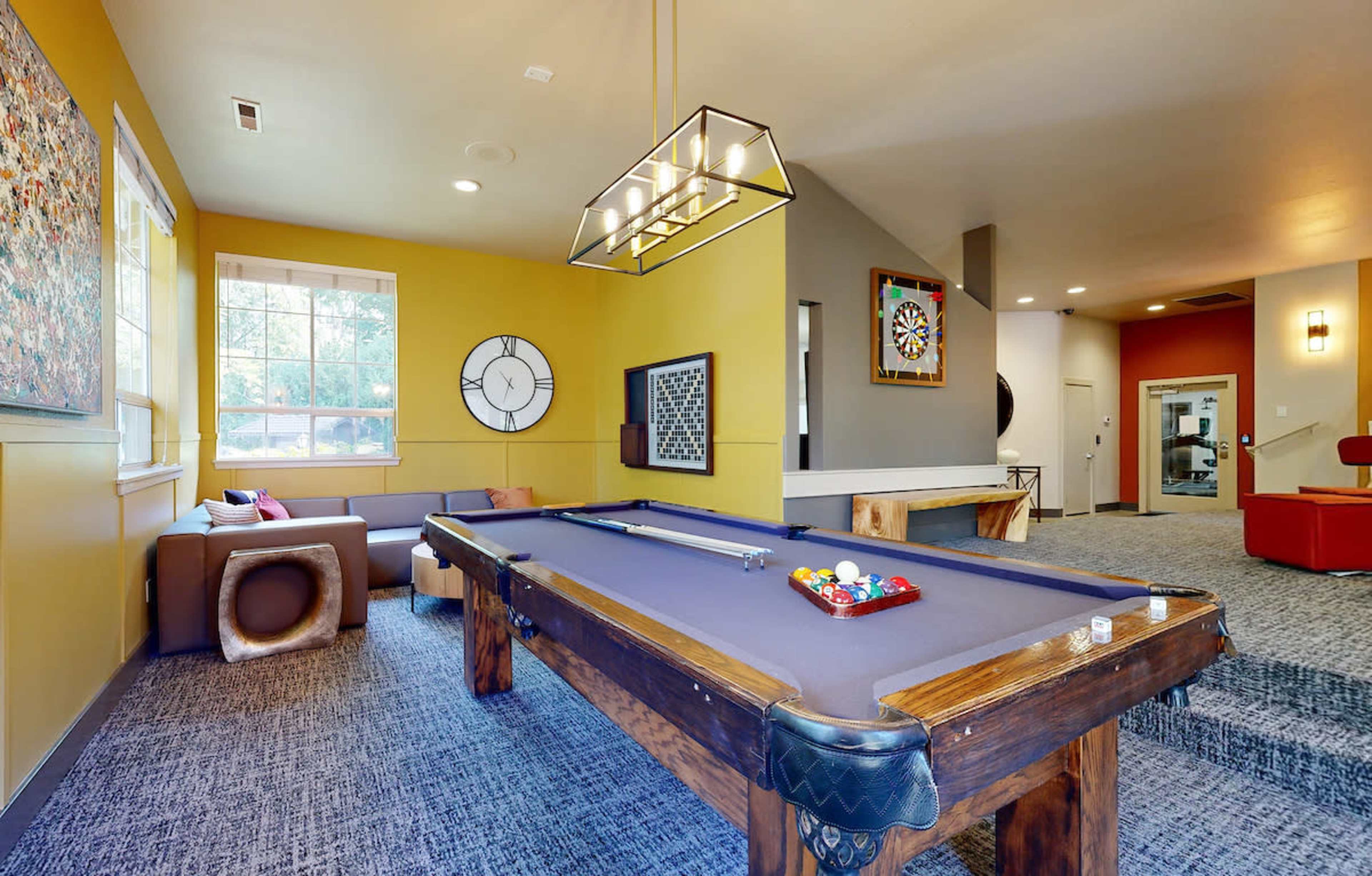 A game room featuring a blue pool table, casual seating, and decorative wall art.
