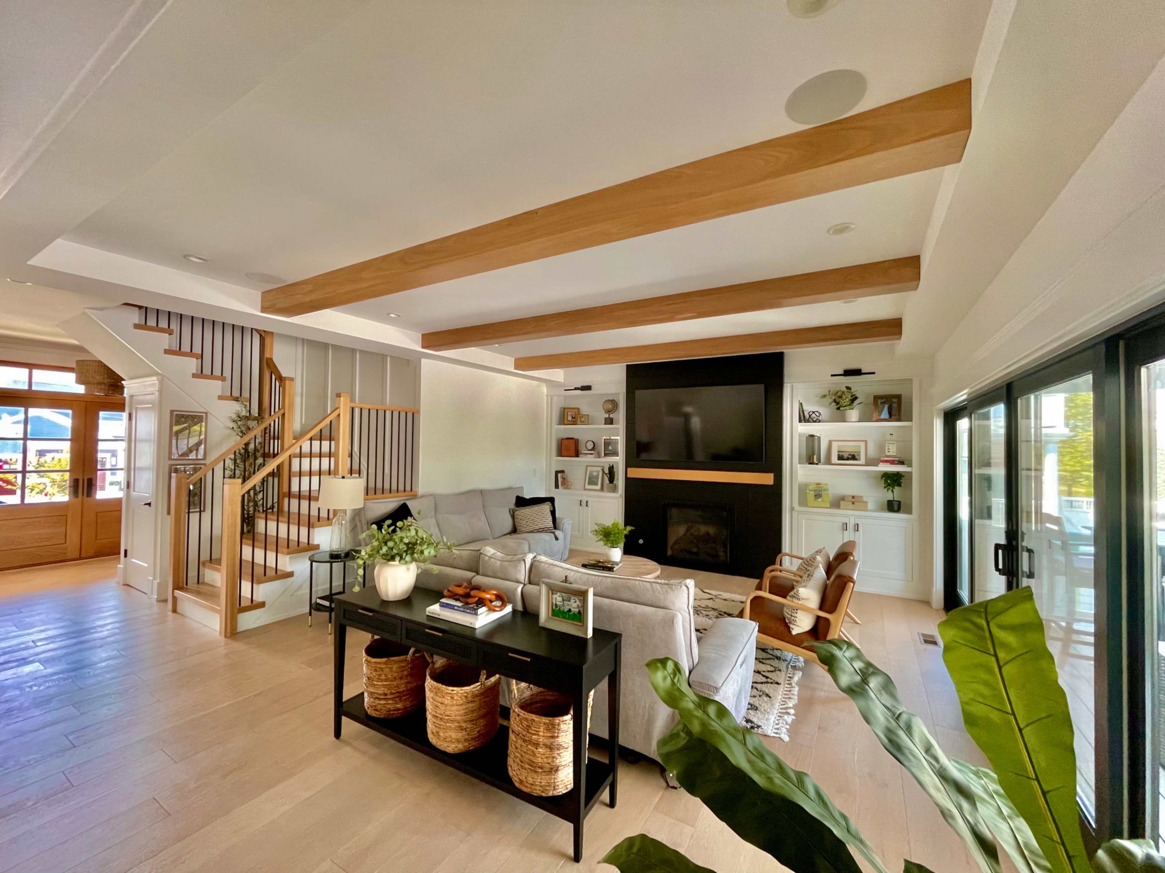 A bright and airy modern living room with exposed wooden beams, a cozy seating arrangement, and a staircase leading to the upper level.