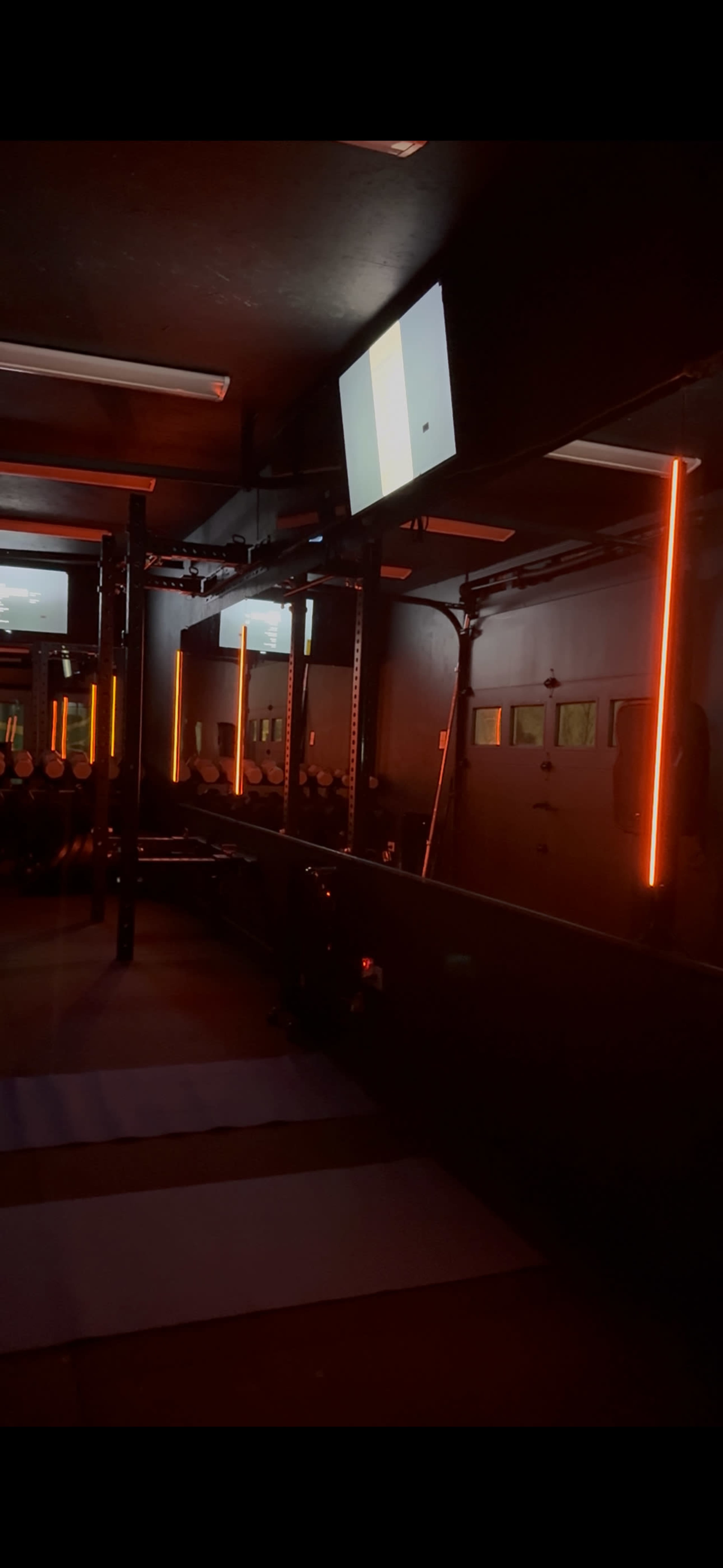 The image shows a dimly lit gym interior with orange neon lights and mirrors, reflecting the workout area and equipment.