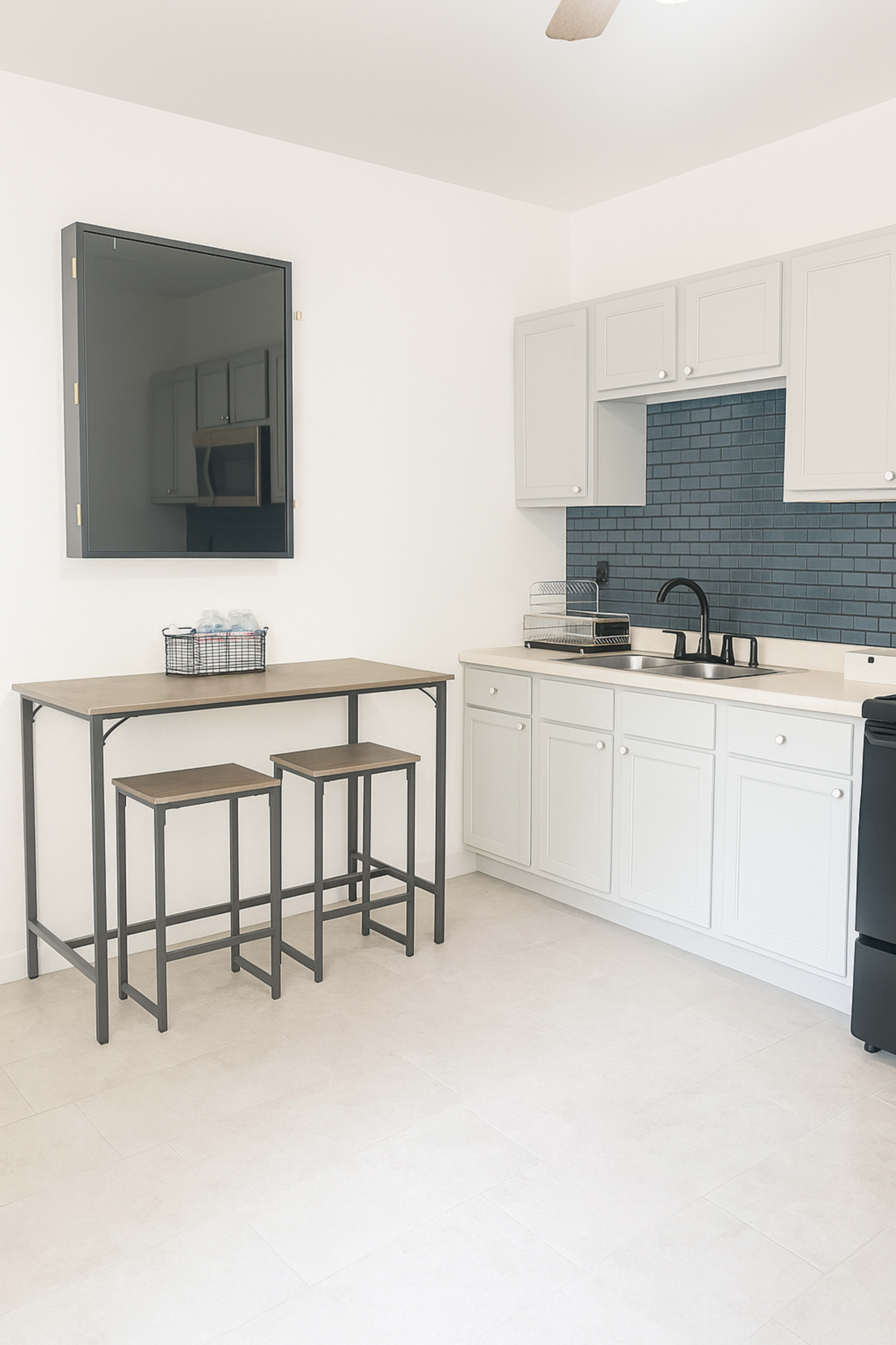 A modern kitchen features a table with two stools, white cabinetry, and a blue tiled backsplash.