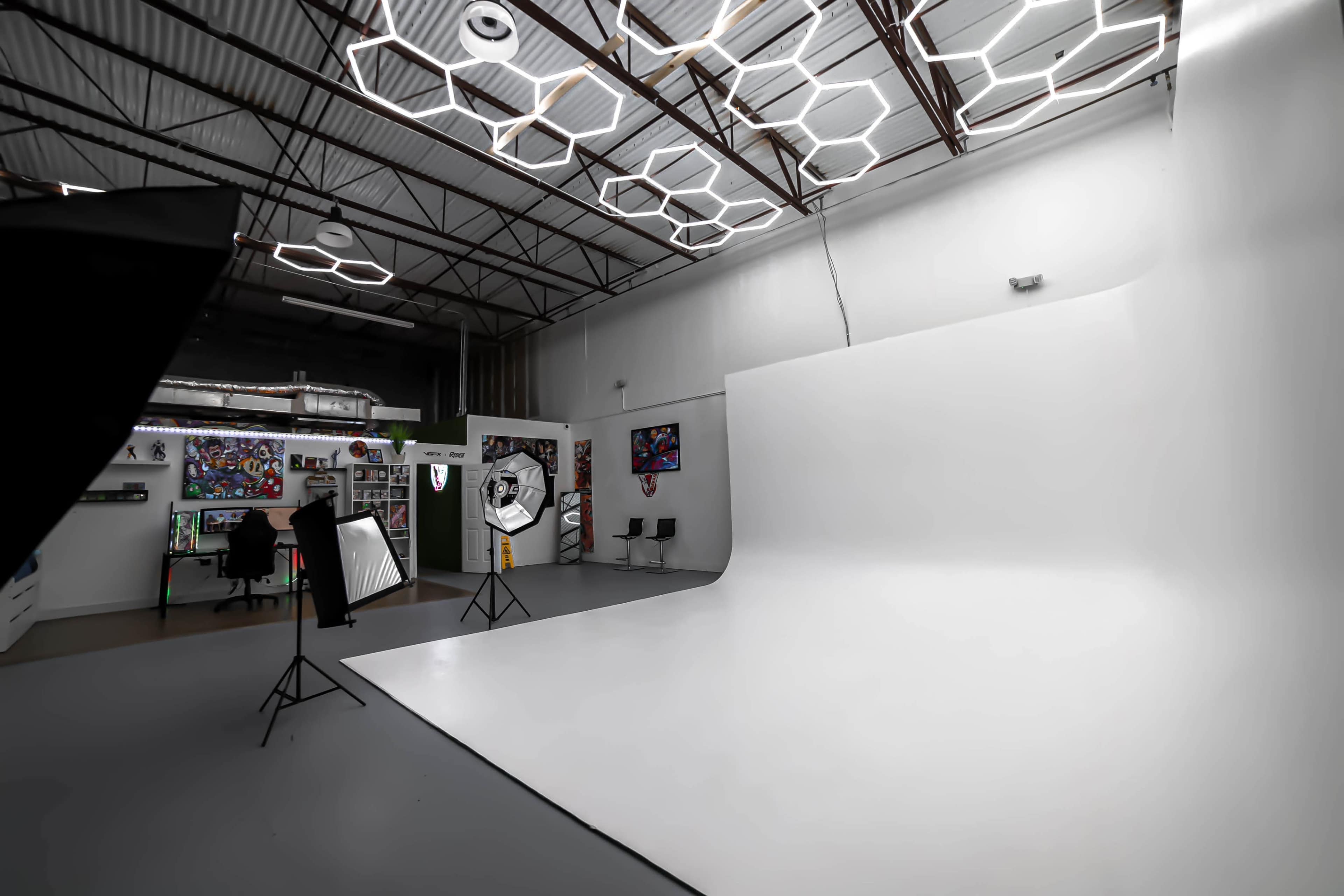A photography studio featuring a large white backdrop, studio lights, and modern hexagonal ceiling fixtures.