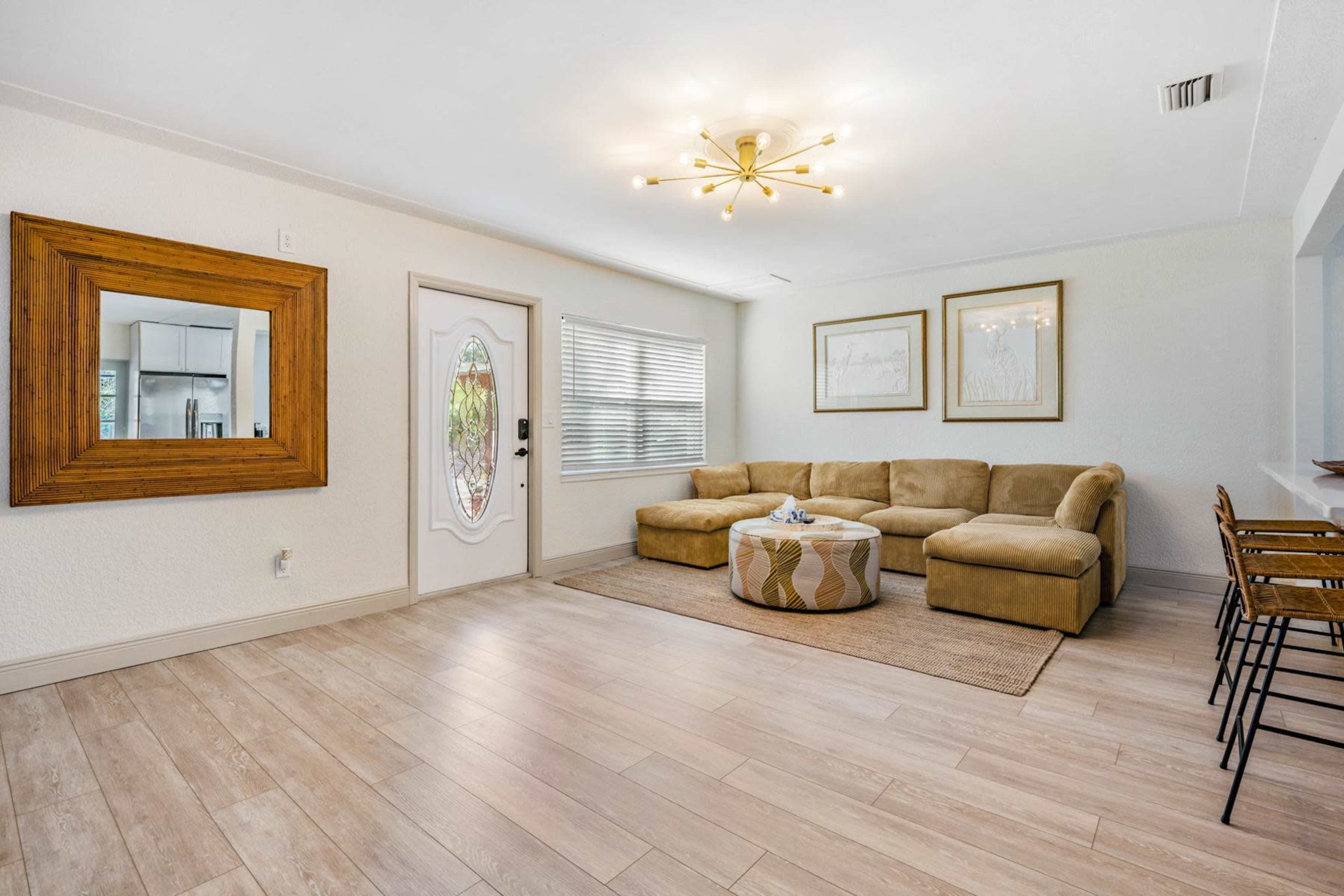 A living room with a beige sectional sofa, a round coffee table, a large mirror, and framed artwork on the walls.