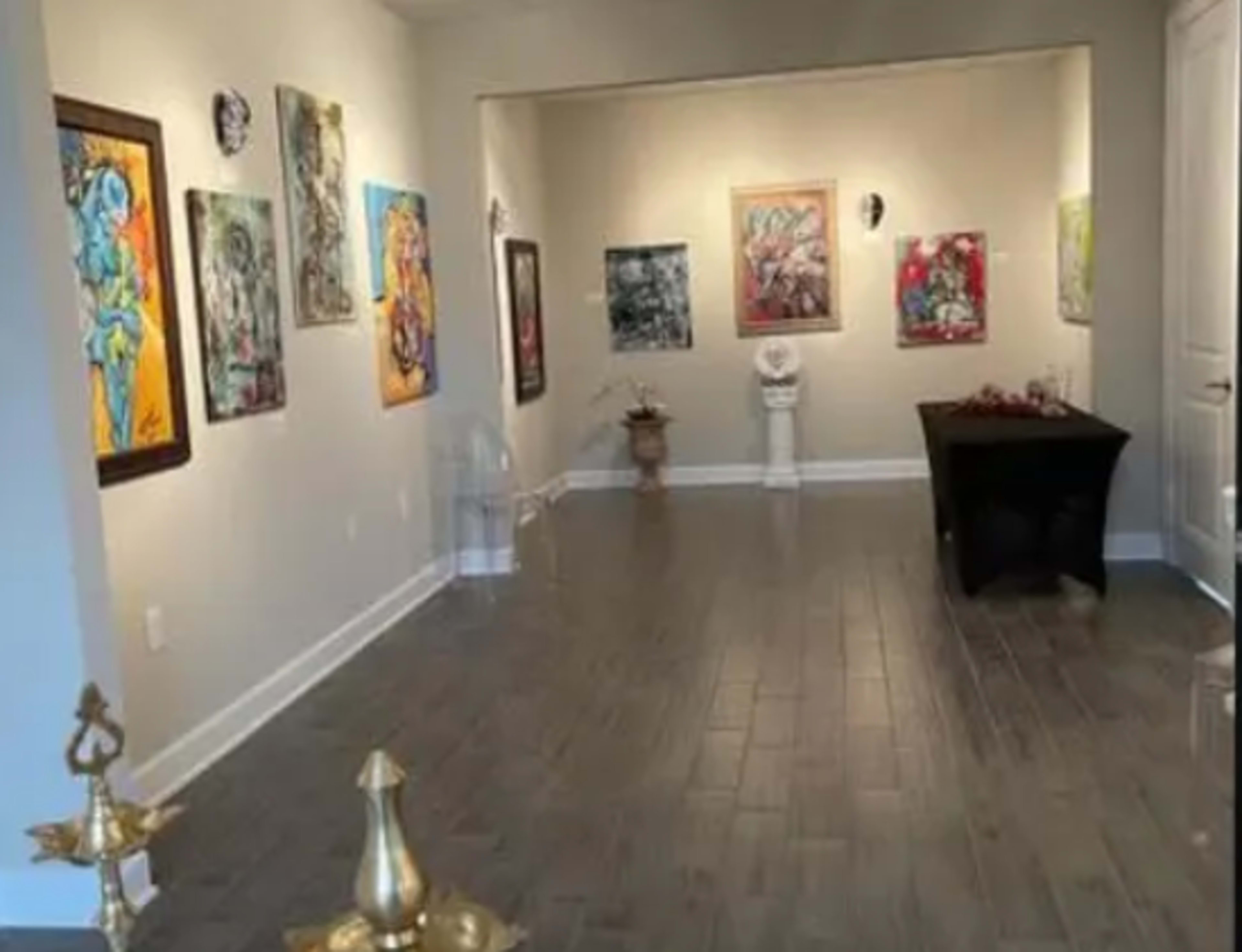 The image shows an art gallery with colorful paintings displayed on the walls and a table in the center of the room.