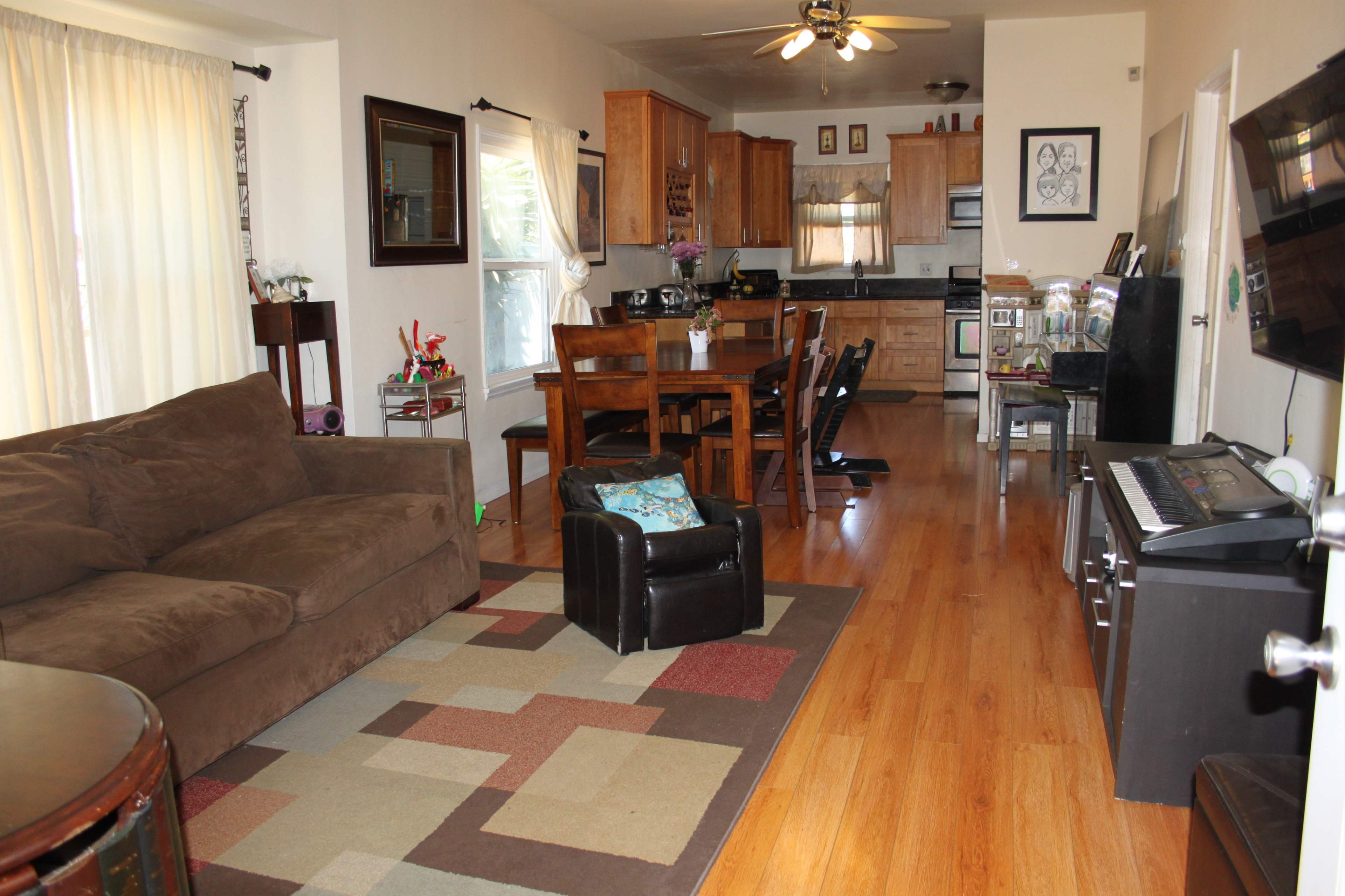 A living room area adjoining a kitchen, featuring a couch, dining table, and various furniture on hardwood floors.