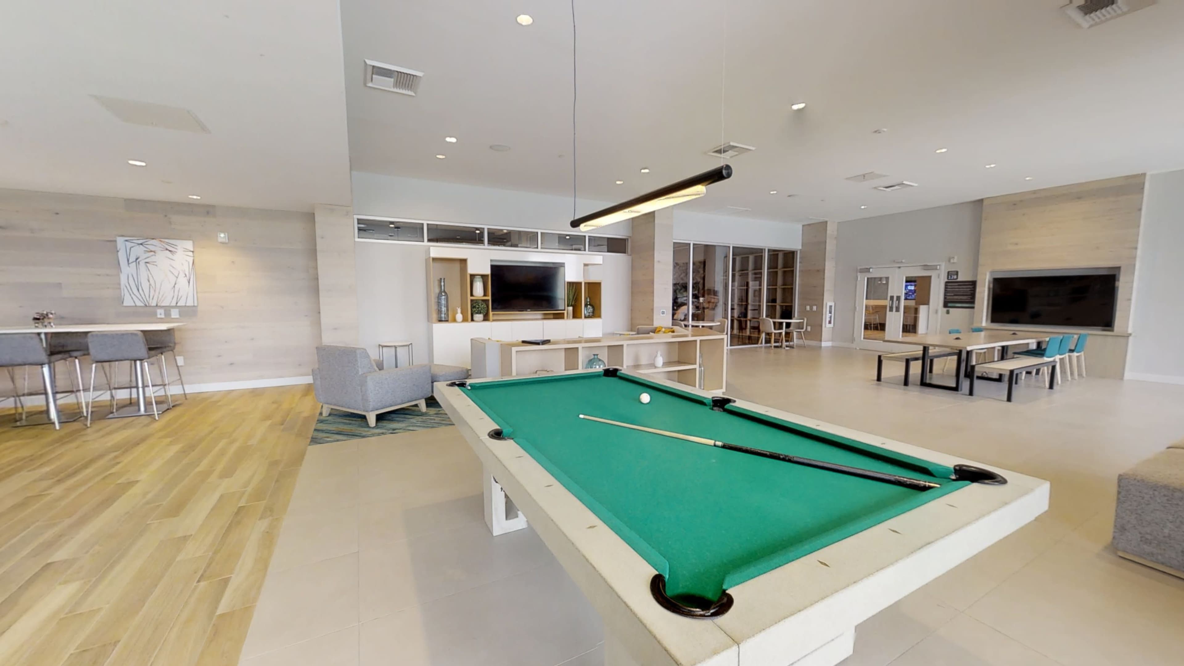 A spacious lounge area featuring a green pool table, seating arrangements, and a large wall-mounted TV.