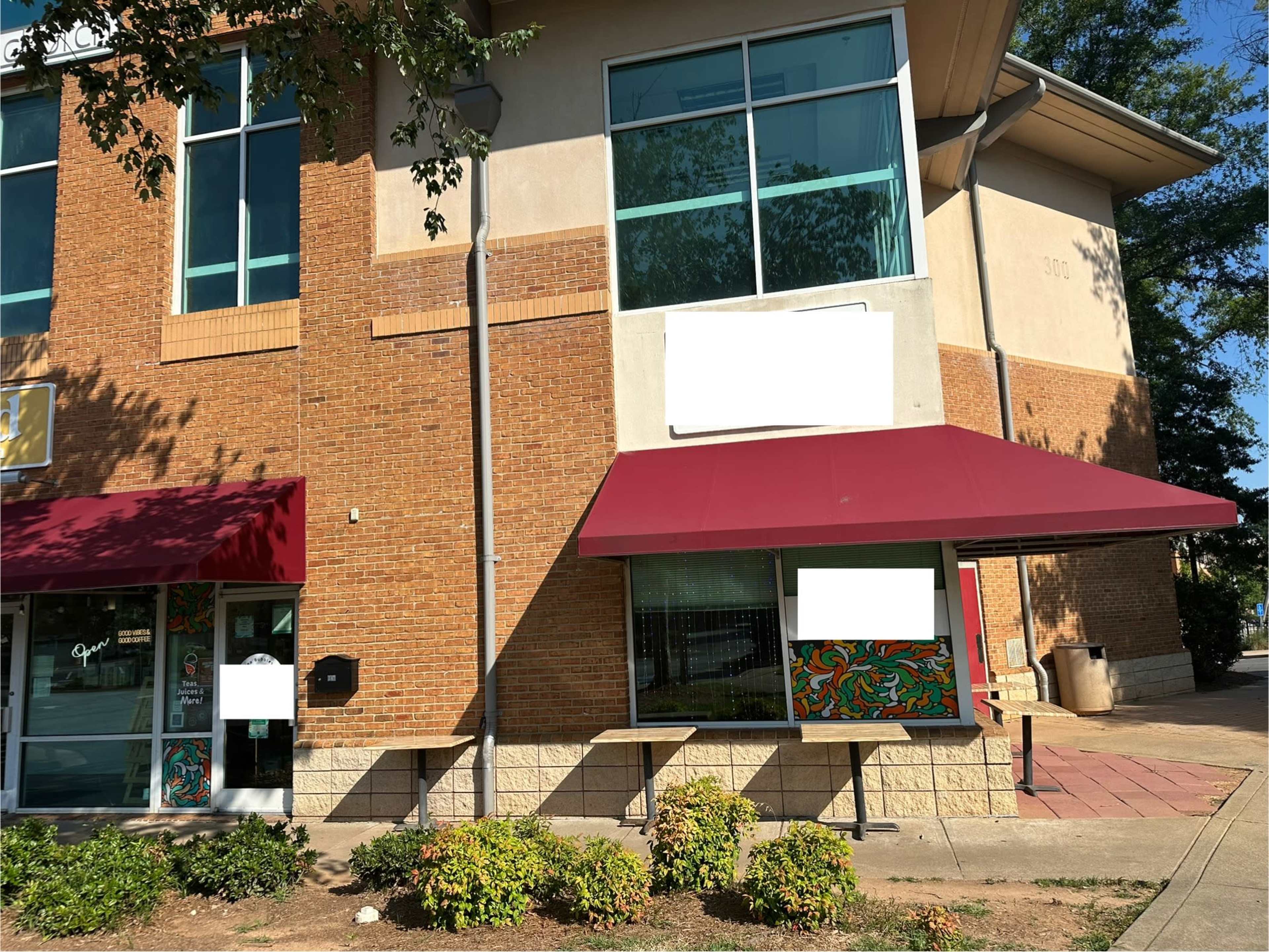 A two-story brick building features large windows and a maroon awning over the entrance.