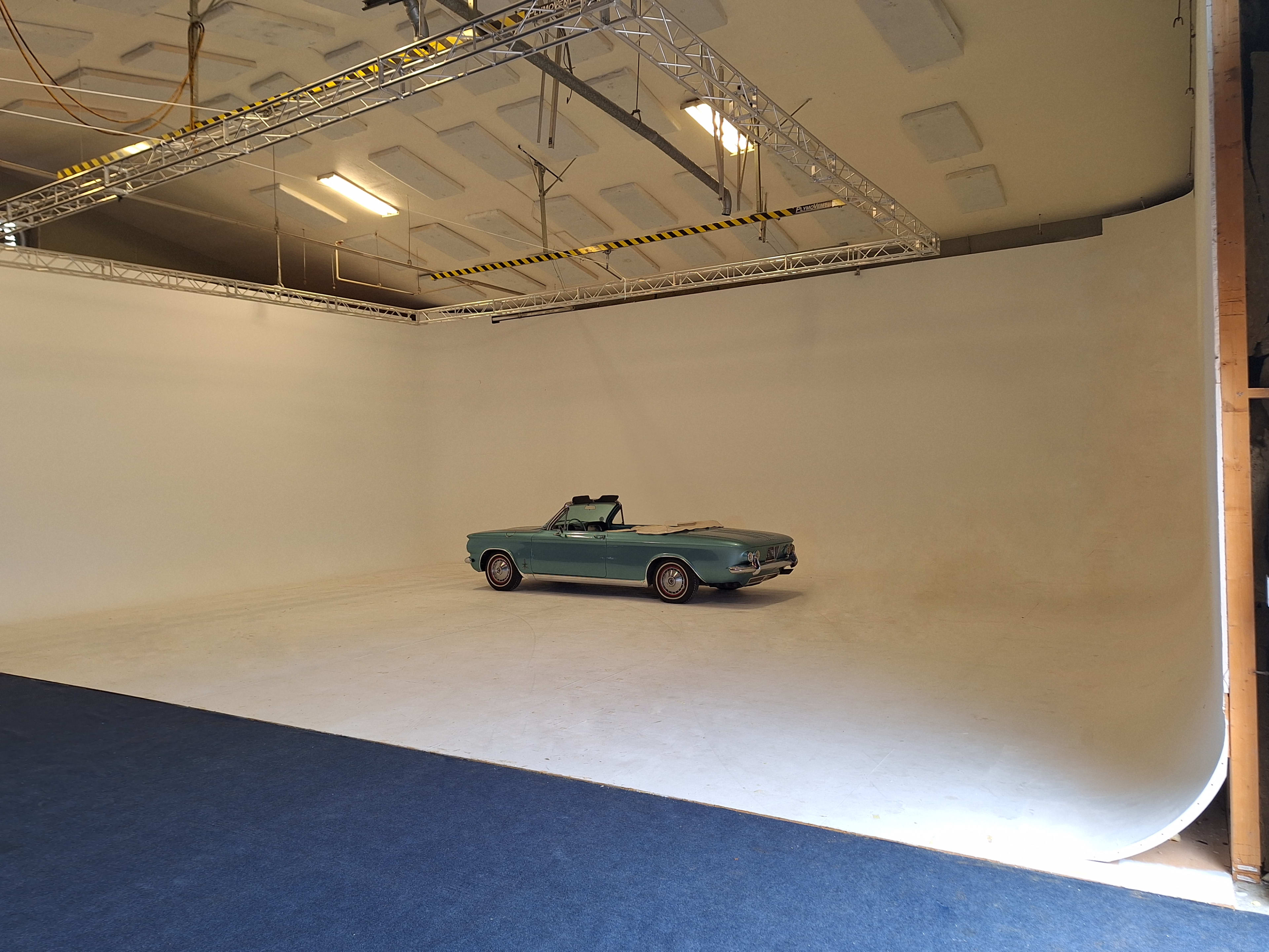A vintage convertible car is positioned on a blank white stage in an empty studio.
