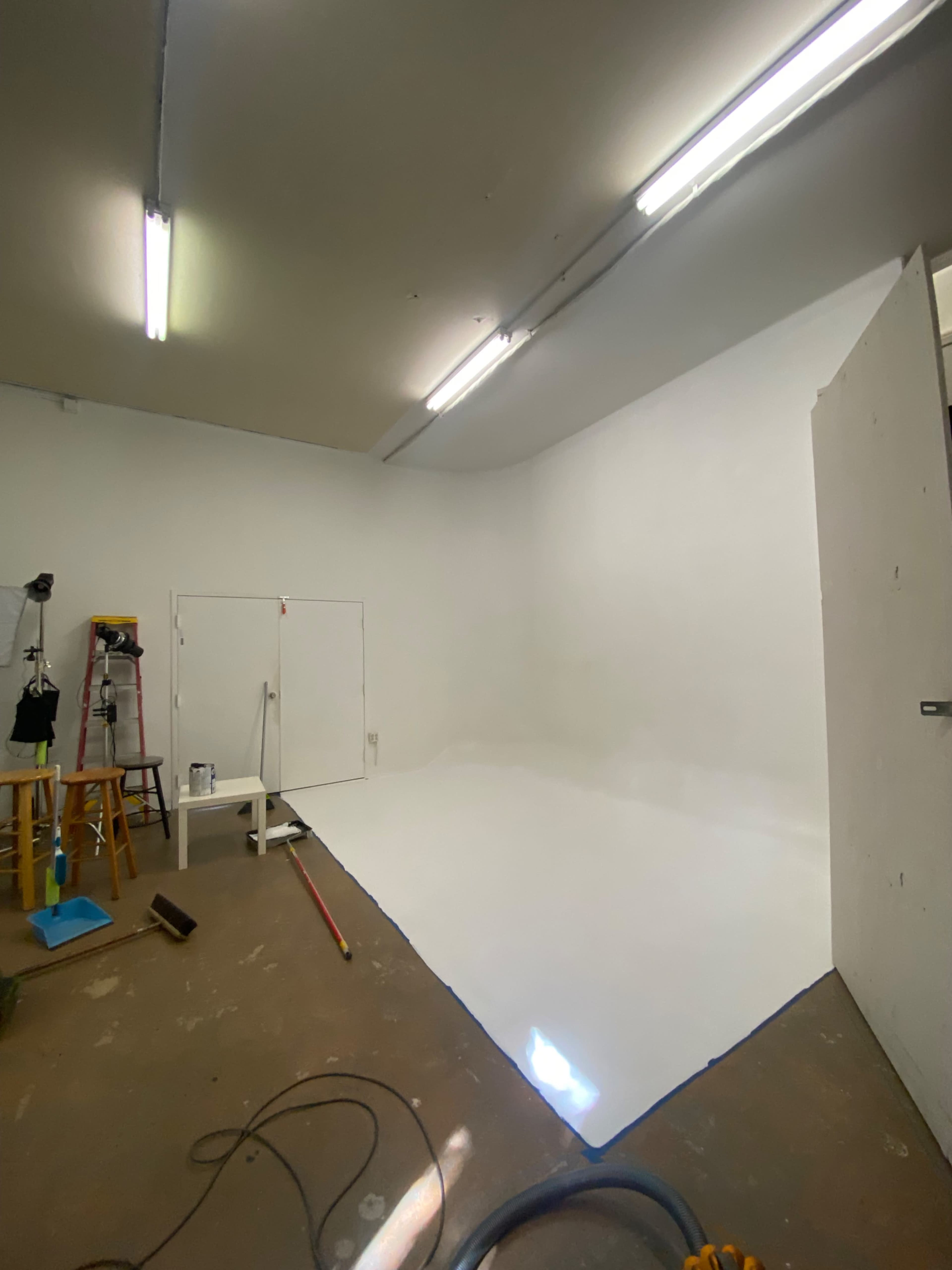 A vacant studio space with white walls and a painted floor, illuminated by overhead lights.