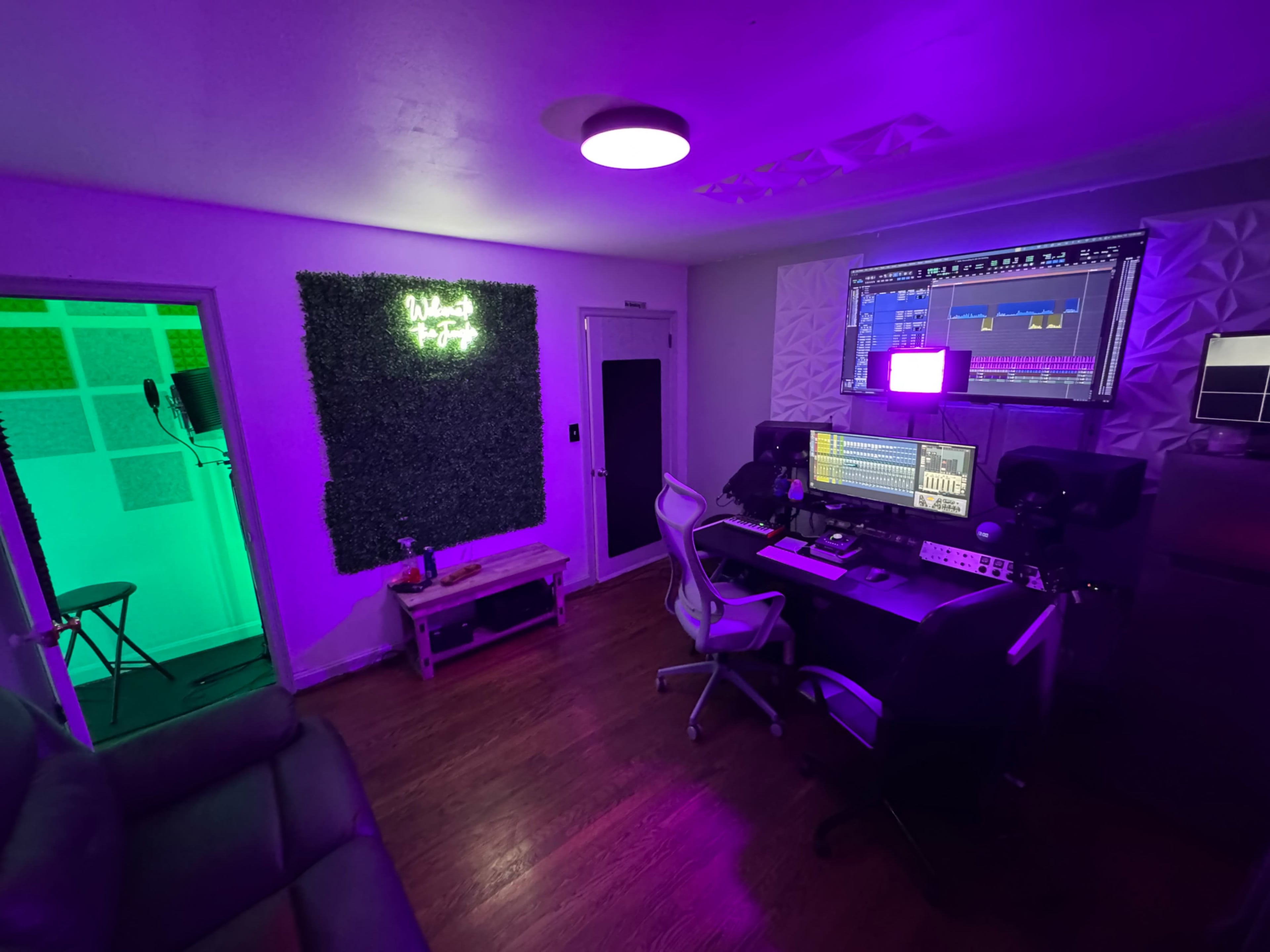 The image shows a music production studio with a desk equipped with monitors, audio equipment, and colorful LED lighting.