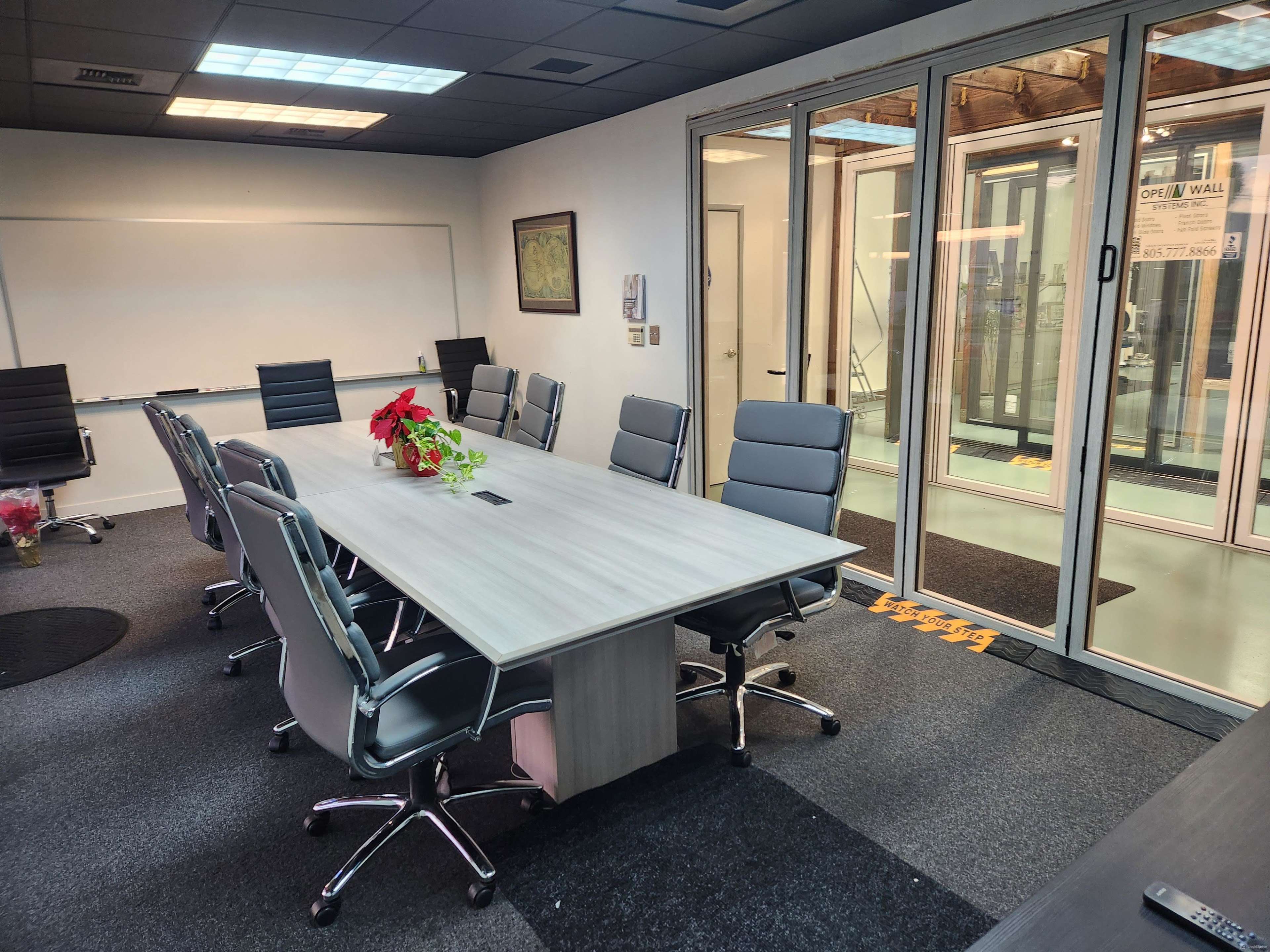 The image shows a modern conference room with a long table surrounded by office chairs and large glass doors leading to an outdoor area.