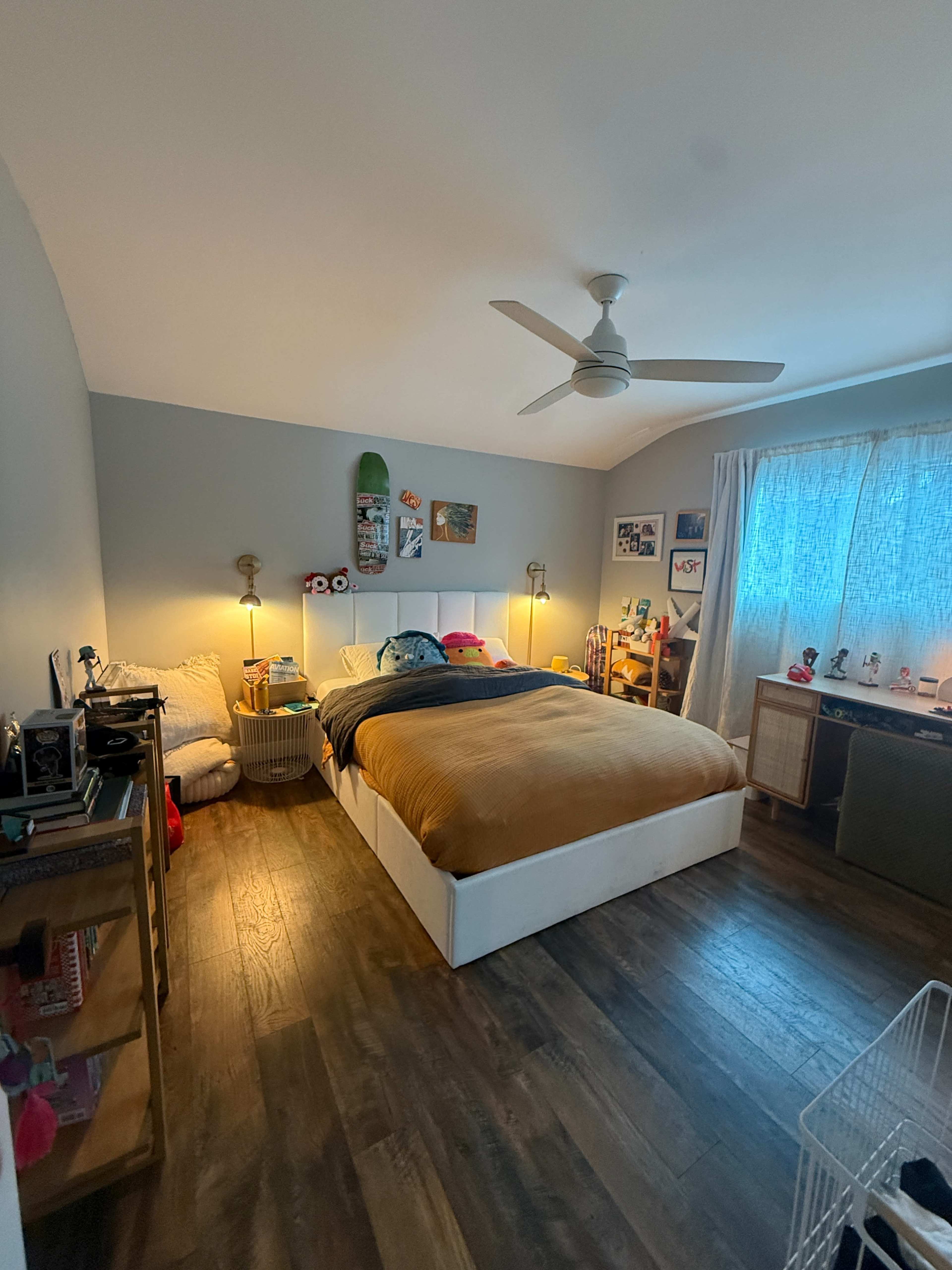 The image shows a well-organized bedroom featuring a large bed with a brown bedspread, two bedside lamps, and various decorations on the walls.