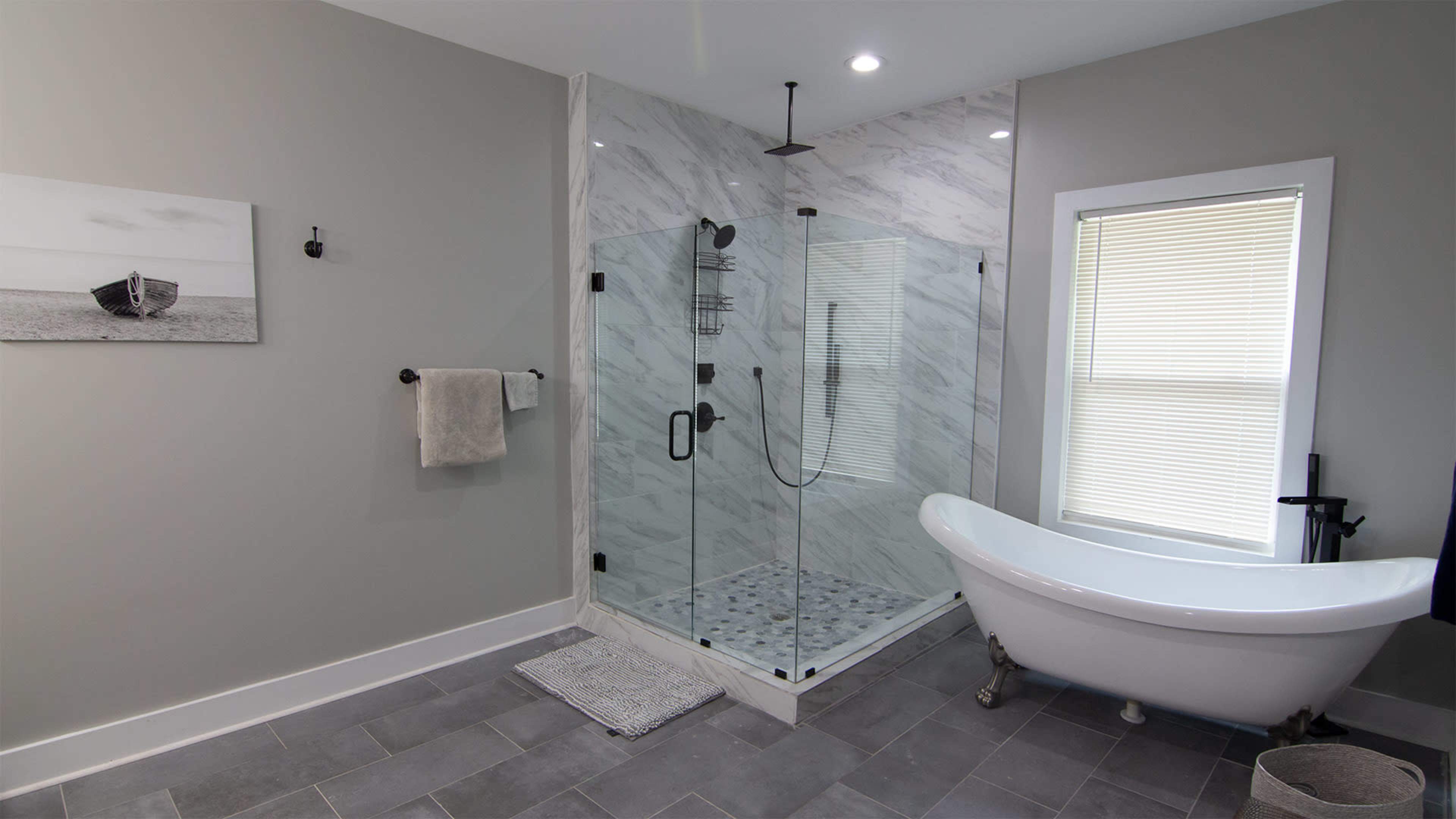 A modern bathroom featuring a glass shower enclosure, a freestanding bathtub, and neutral-colored walls and tiles.