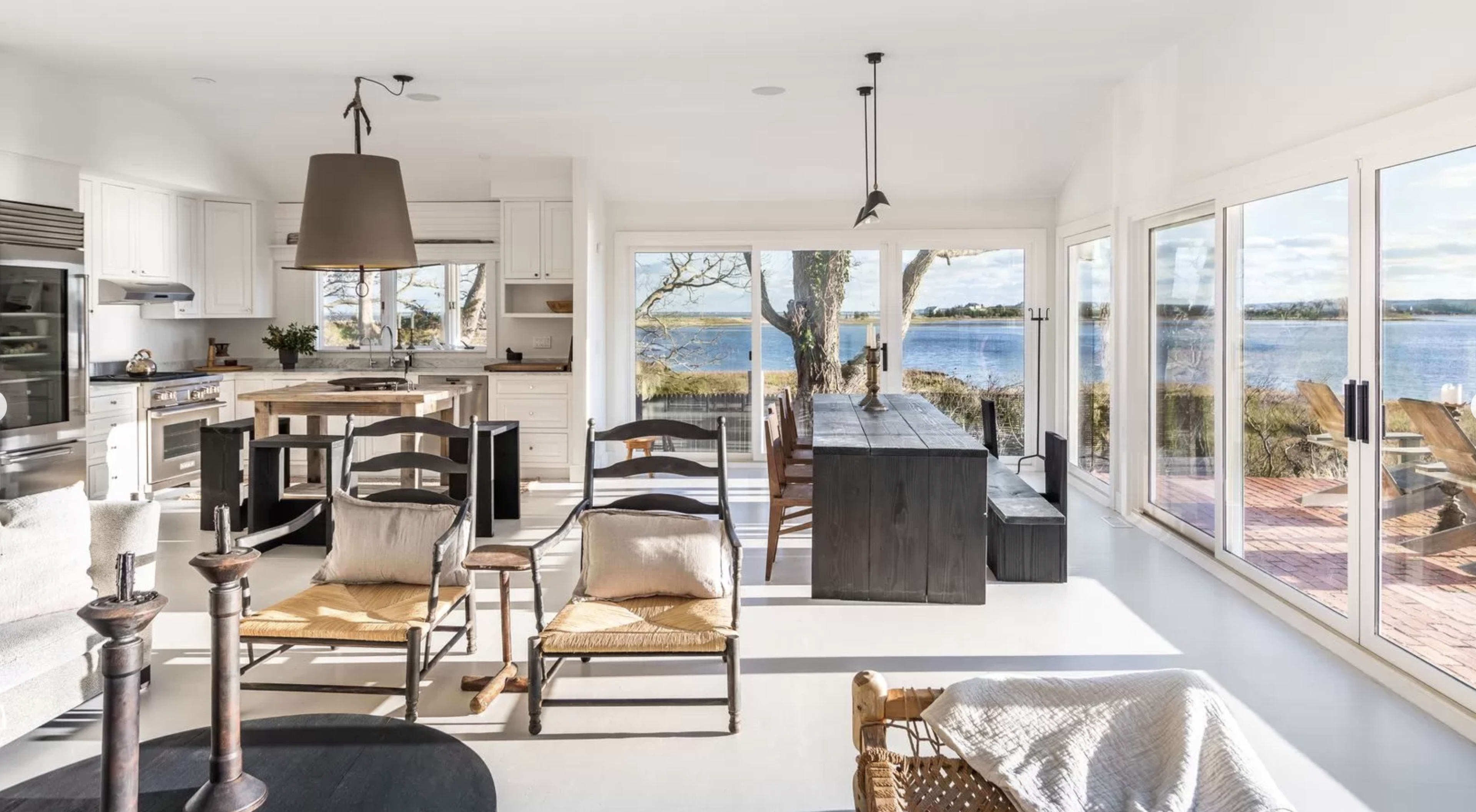 A bright, modern living space features a kitchen, dining area, and large windows that offer a view of the water.
