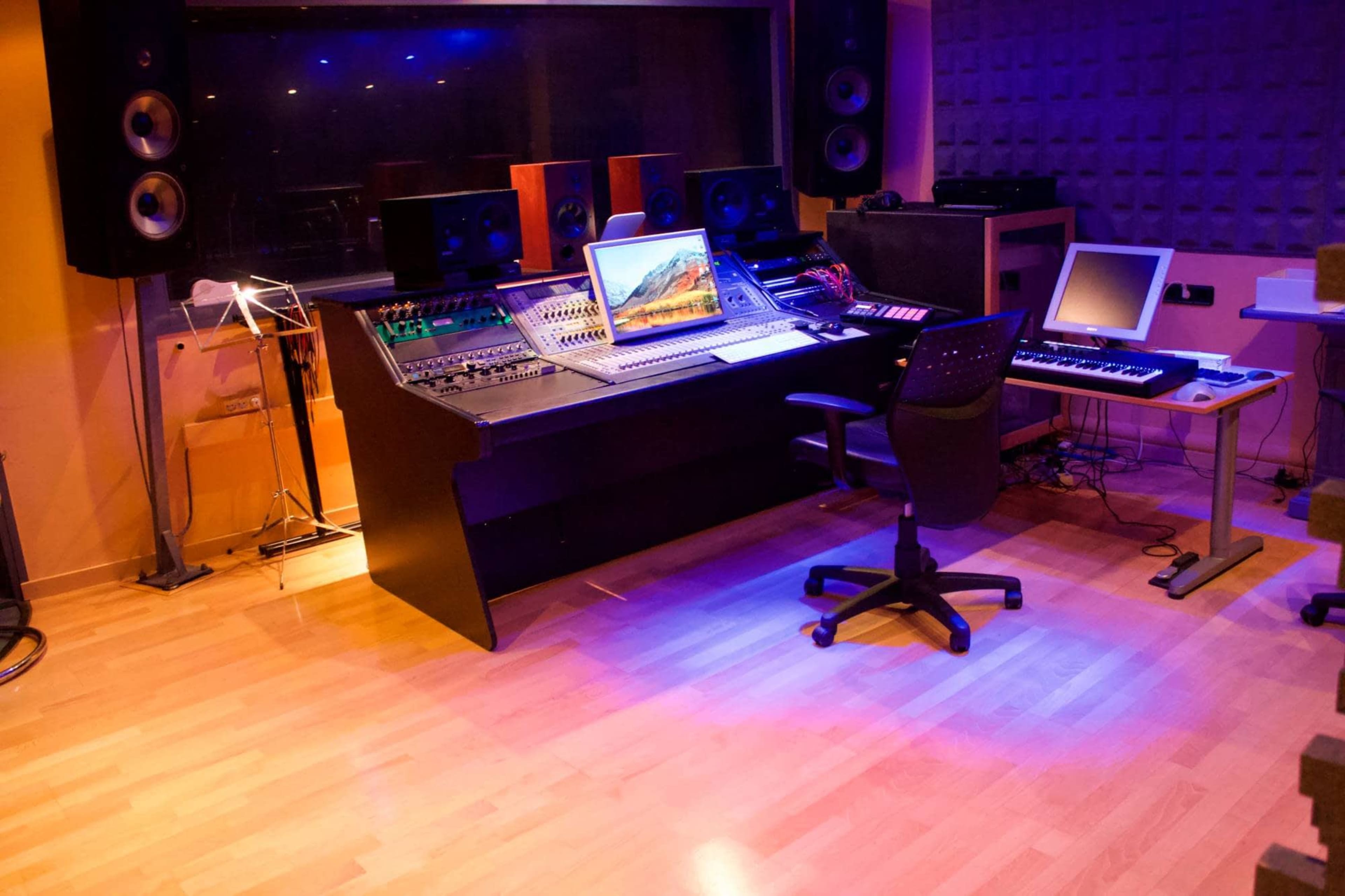 A recording studio with a mixing console, computer, keyboard, and speakers, all arranged in a well-lit space with wooden floors.