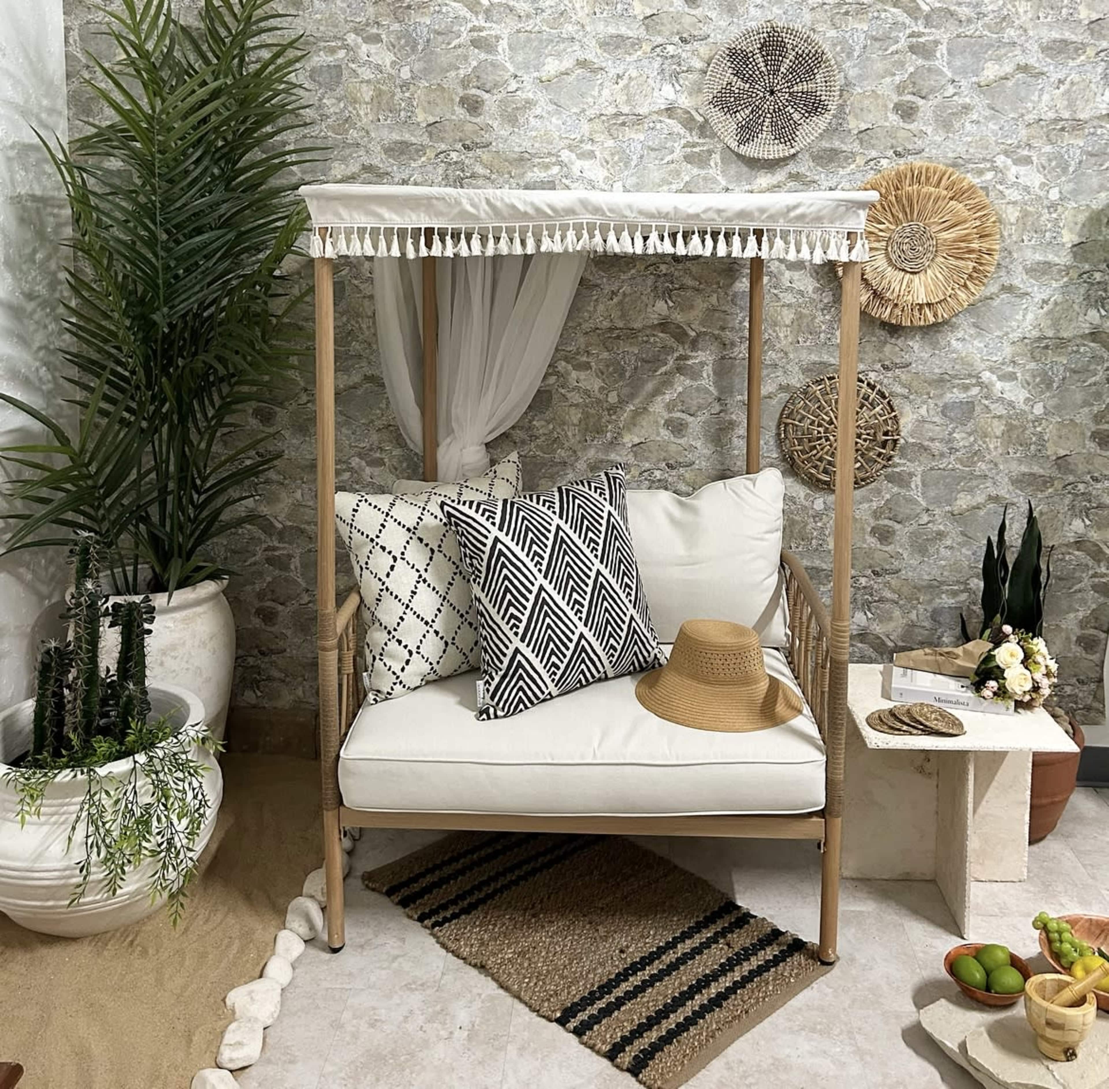 A cozy outdoor seating area features a wooden canopy chair adorned with patterned cushions, surrounded by decorative plants and natural stone walls.