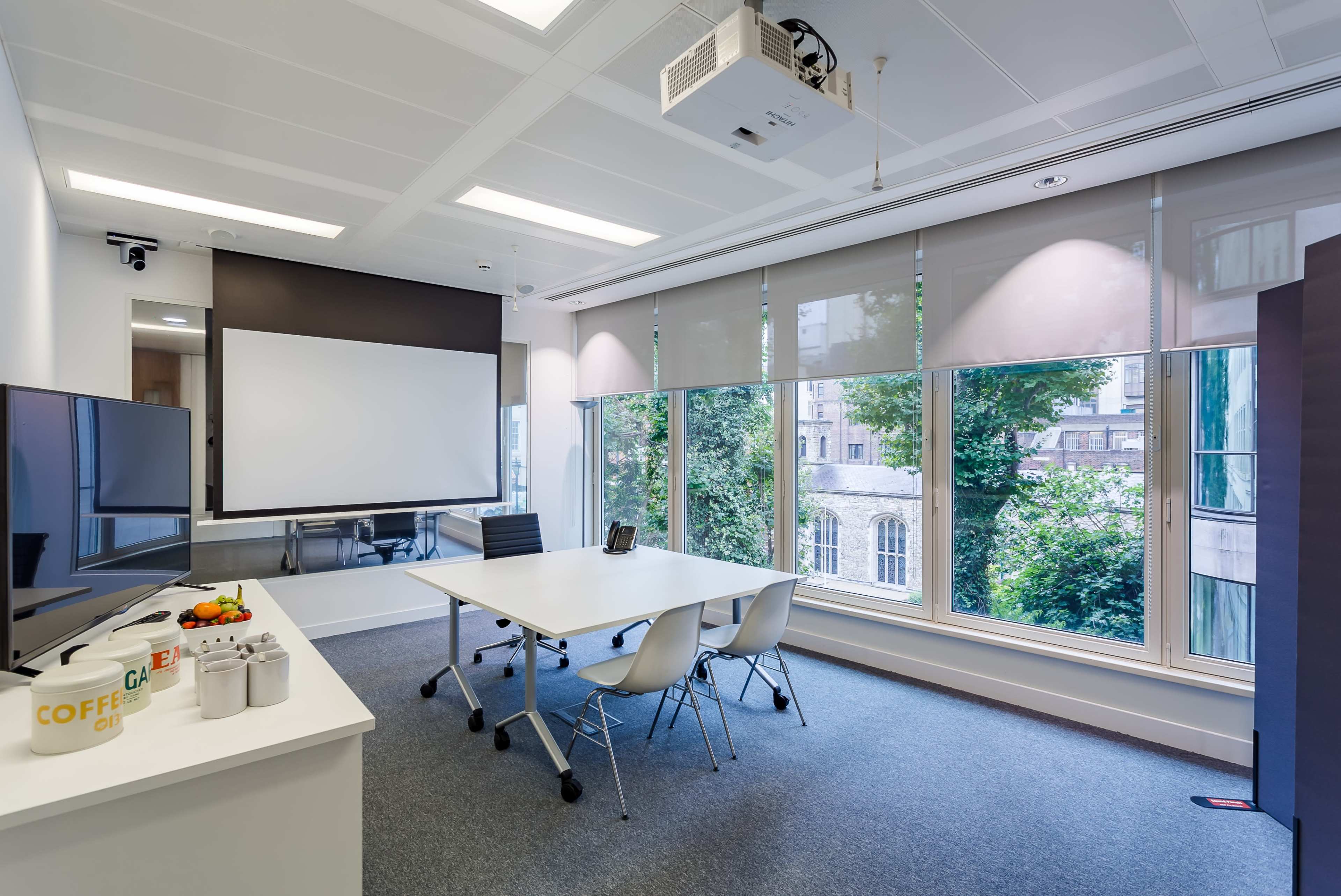 A modern conference room features a large table, a projector screen, and windows with views of greenery.